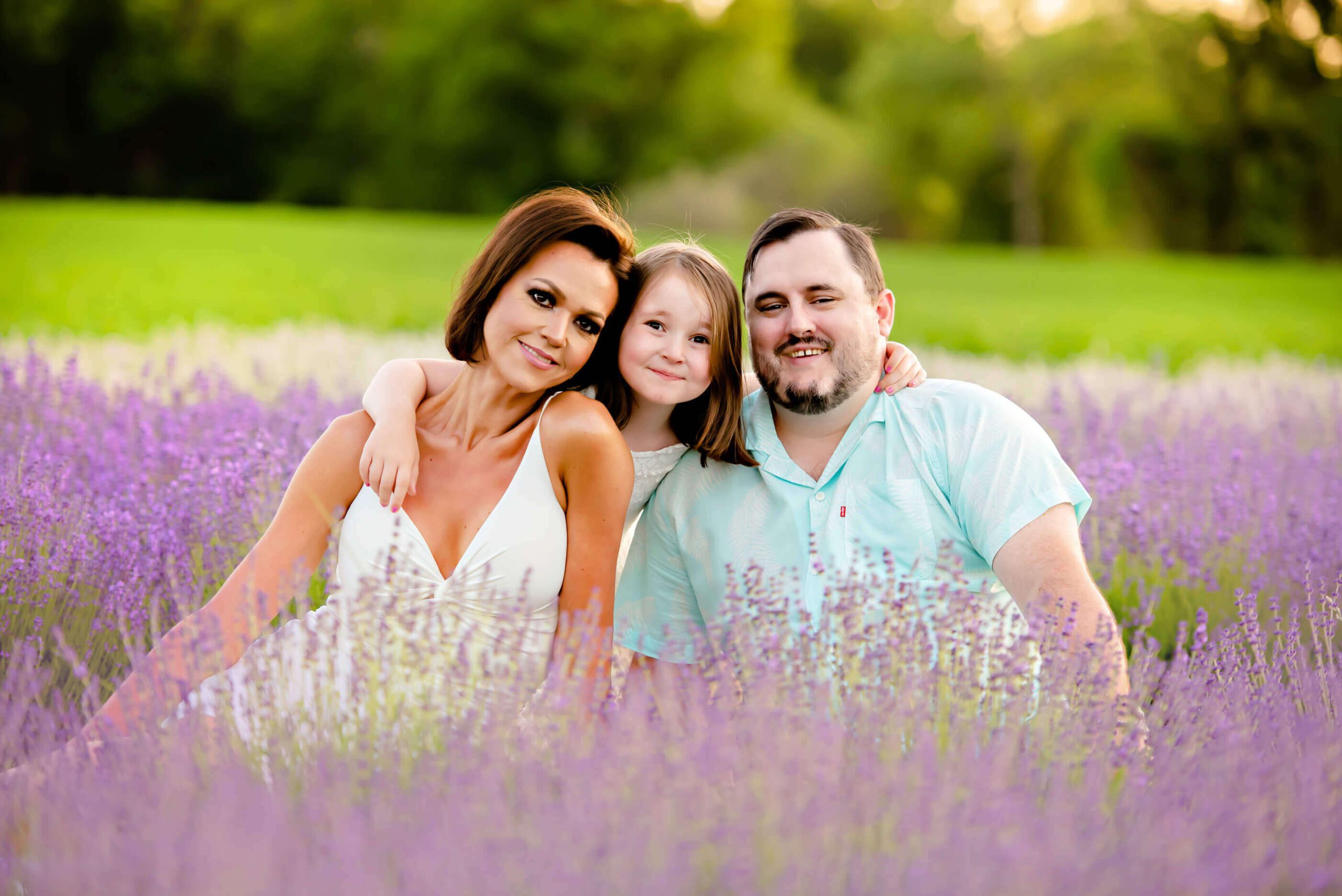 mom and dad with their daughter sitting in the gorgeous lavender field in Ontario