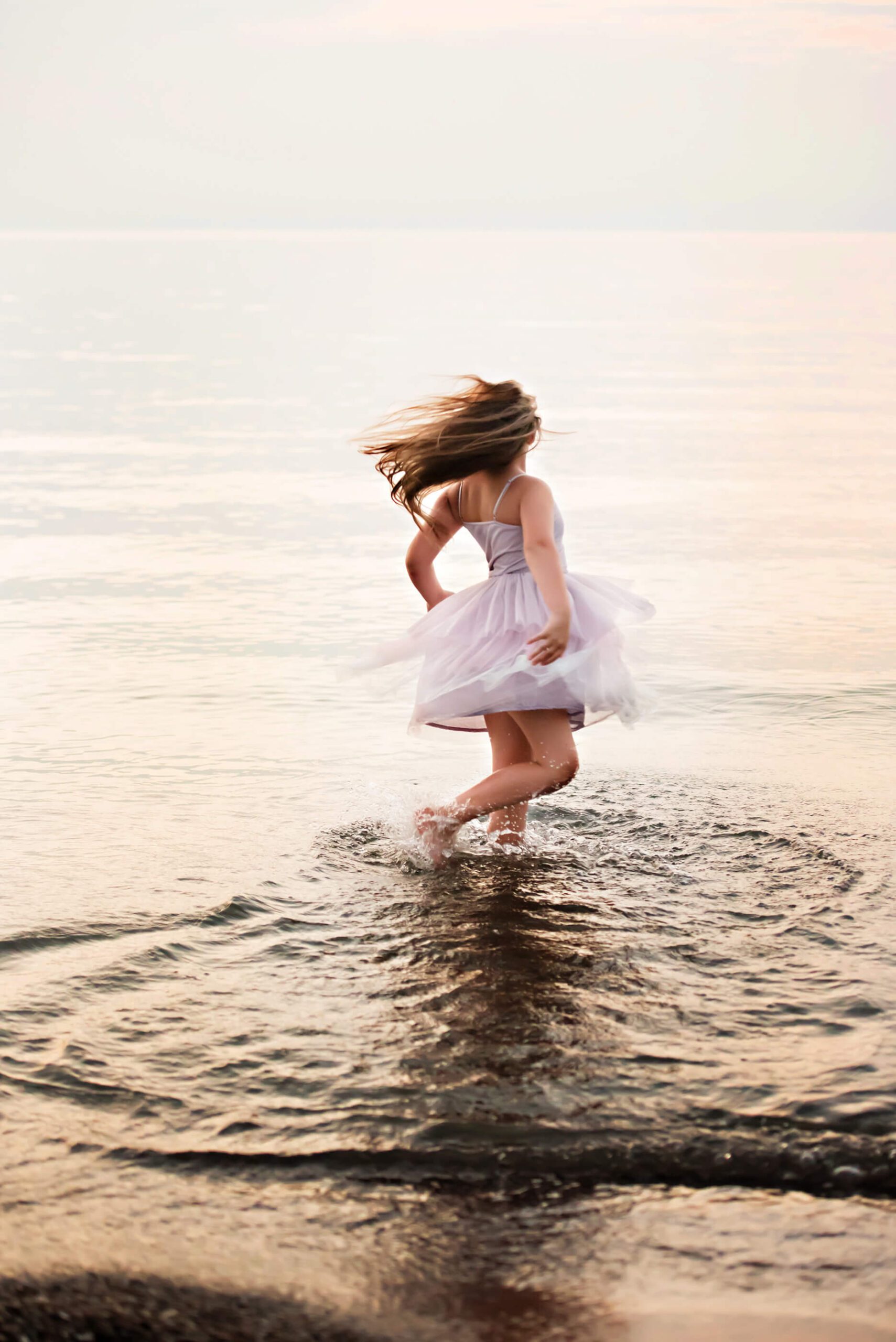 Stunning girl spinning in the water at sunset at the beach. Toronto Splash Pads