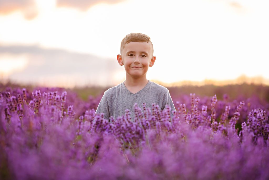 young boy standing in a lavender field smiling