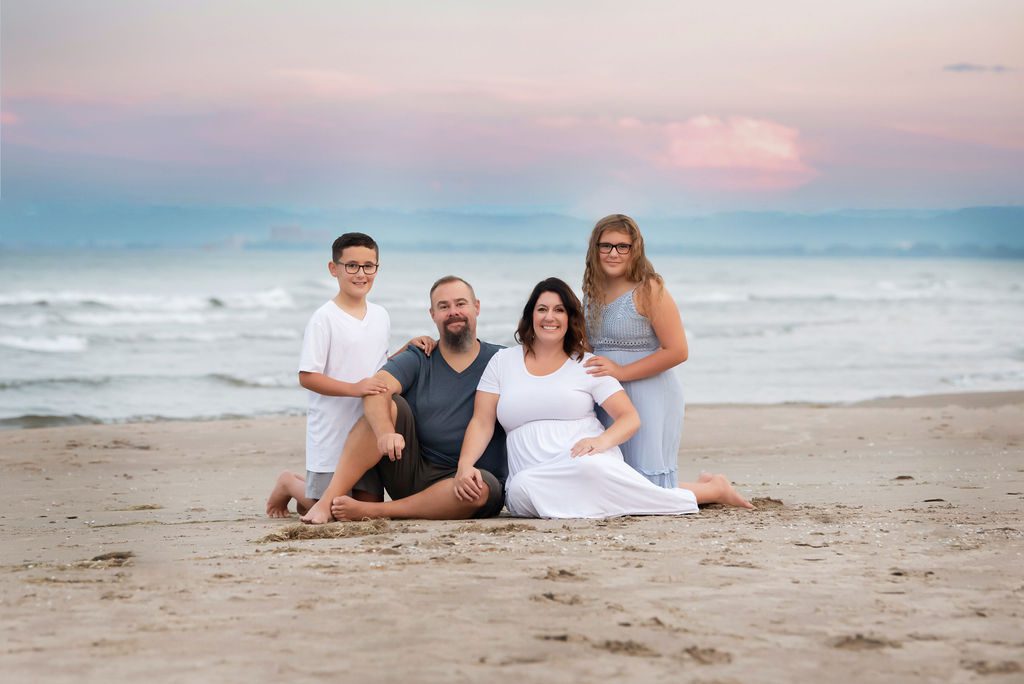 family of four sitting in the sand on the beach at sunset Gynecologists in Burlington Ontario