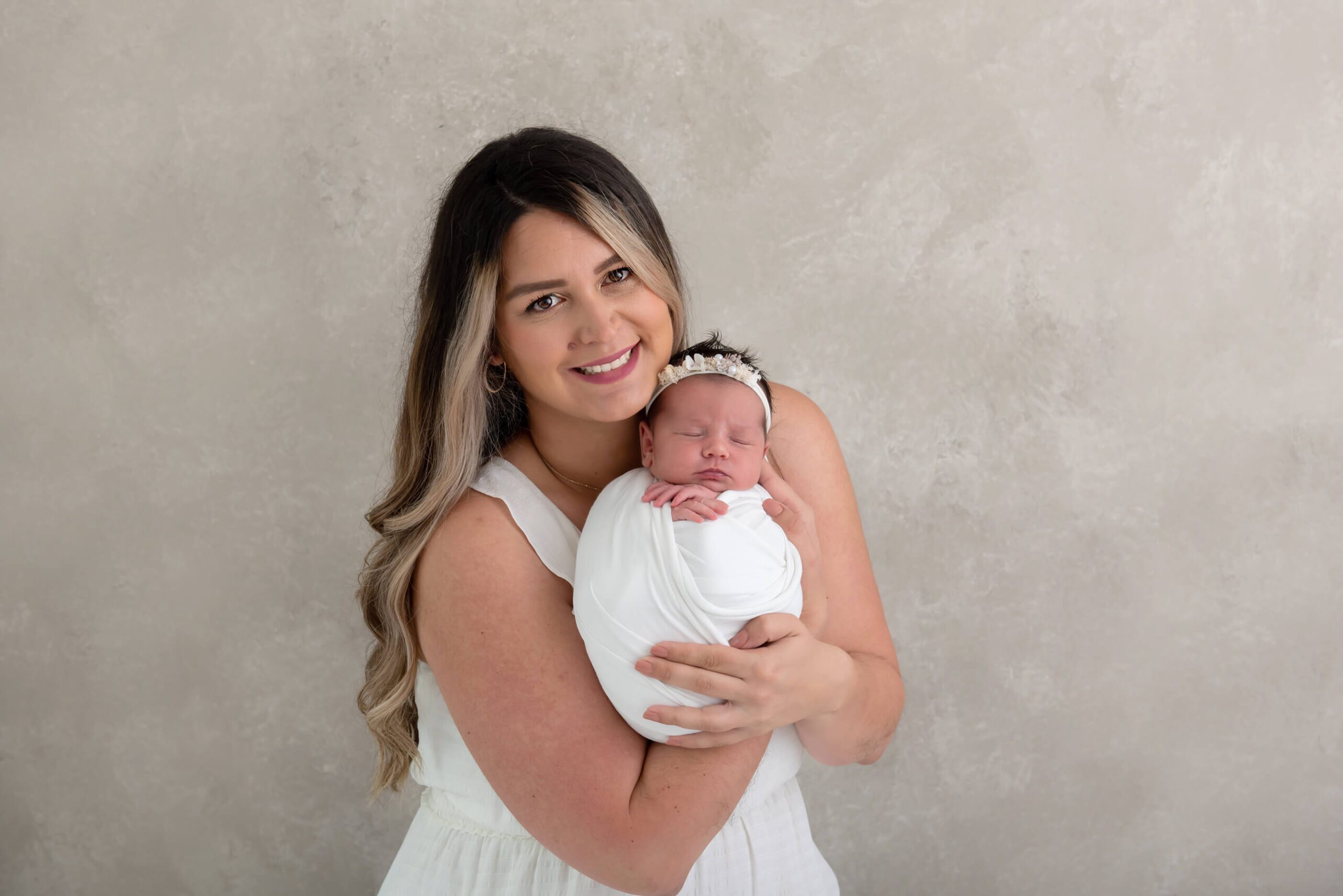mom holding baby newborn girl wrapped in white with a headband