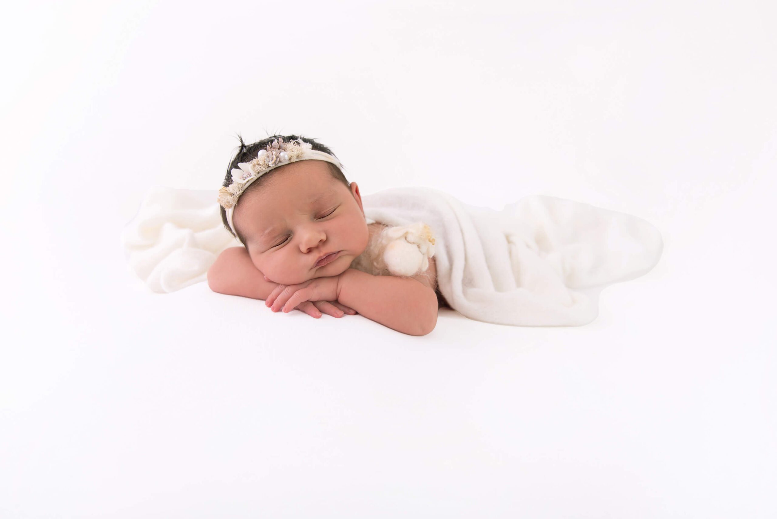 all white newborn baby laying down with a white wrap, headband, holding a lamb Burlington newborn photographer