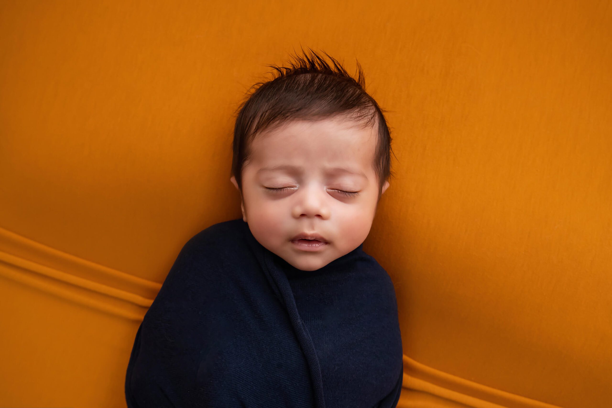 newborn boy wrapped in blue on orange blanket