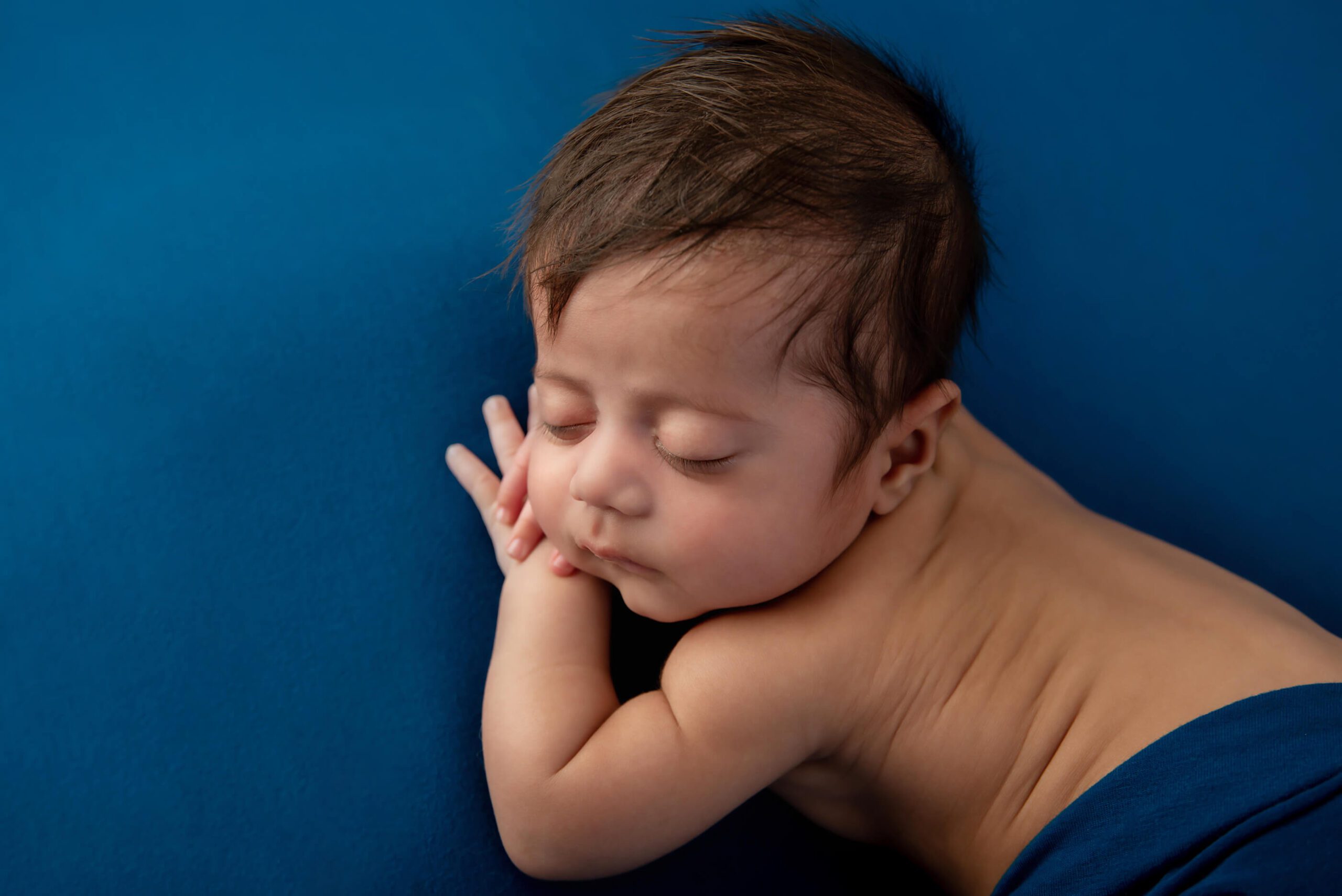 side view newborn baby boy on a blue background Burlington newborn photography