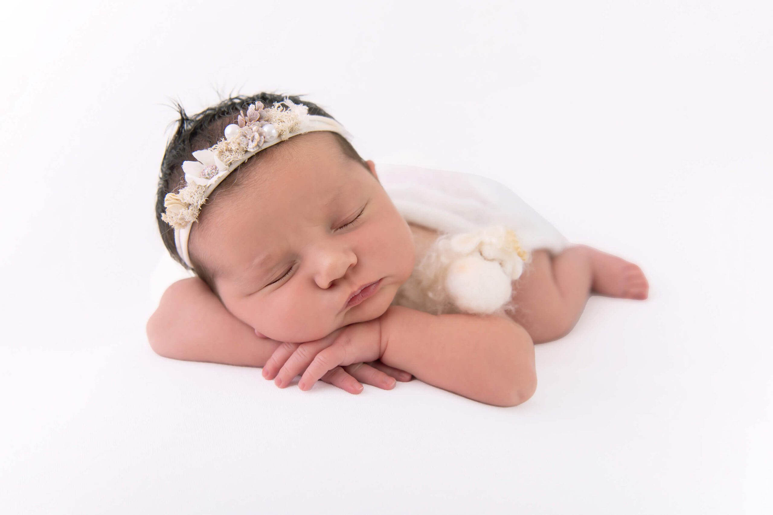 all white newborn baby laying down with a white wrap, headband, holding a lamb Cambridge newborn photography