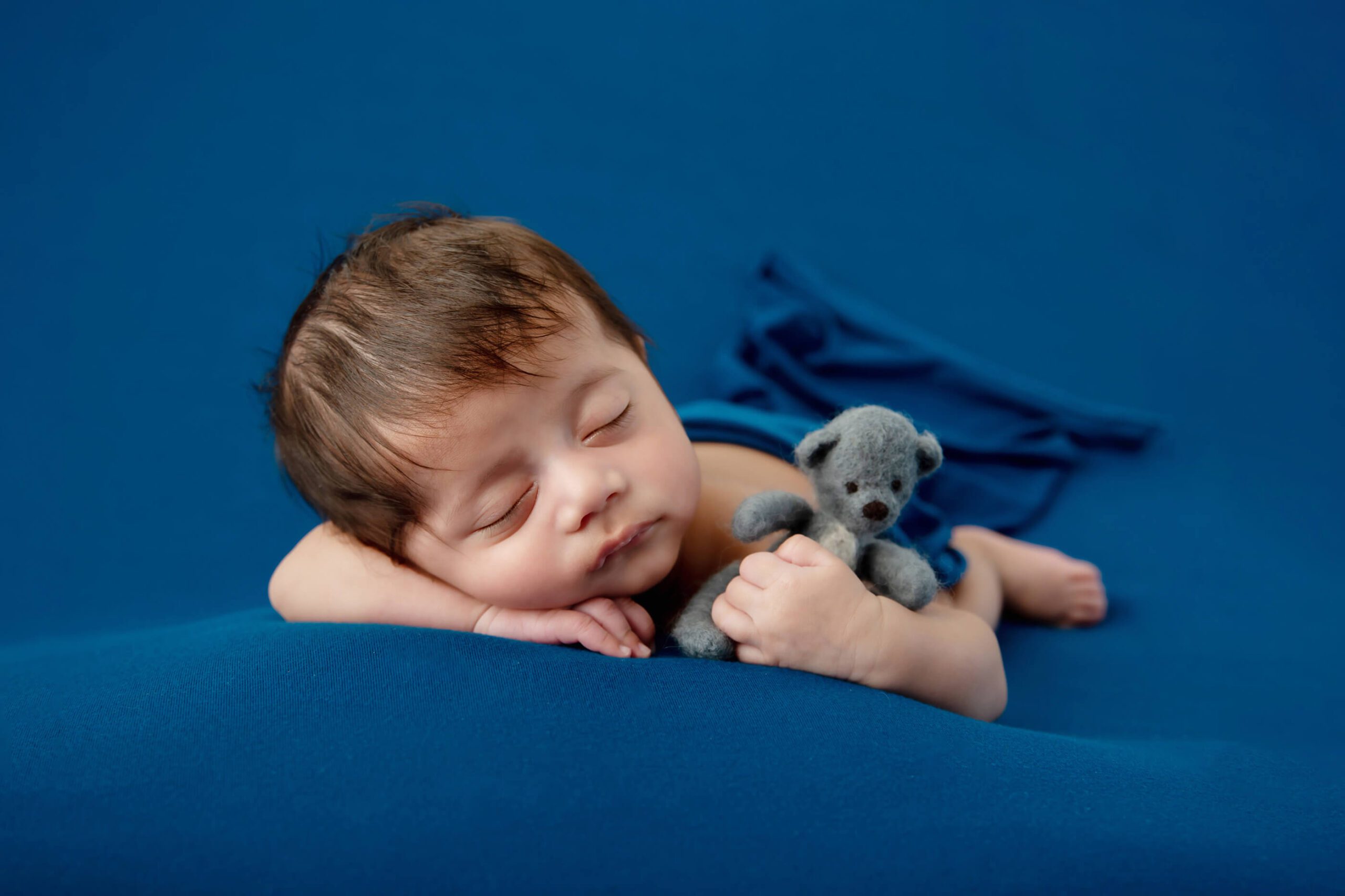 newborn baby boy on a blue background holding a teddybear Cambridge newborn photos