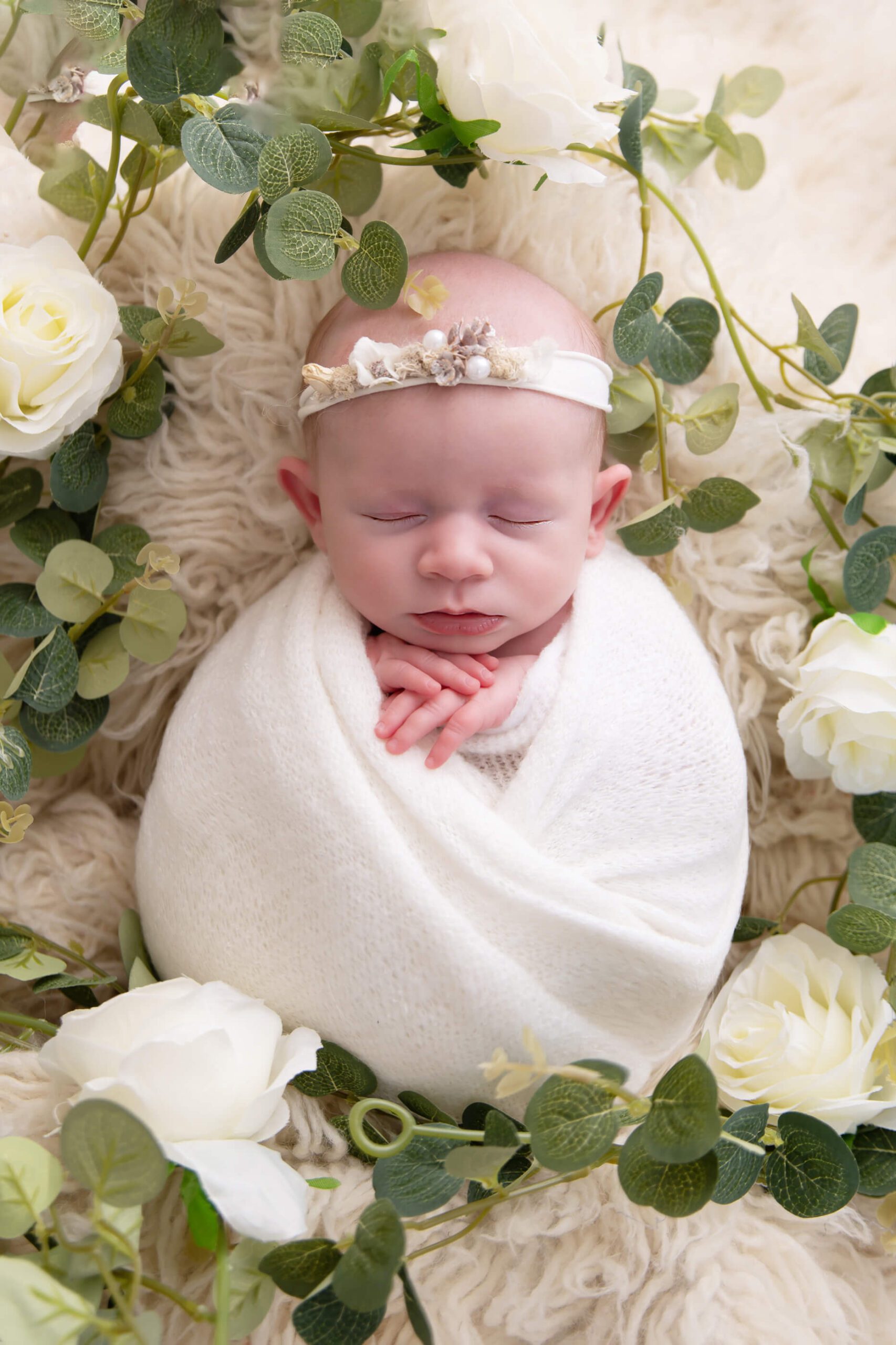newborn girl laying wrapped in white with white flowers around her Cambridge newborn photos