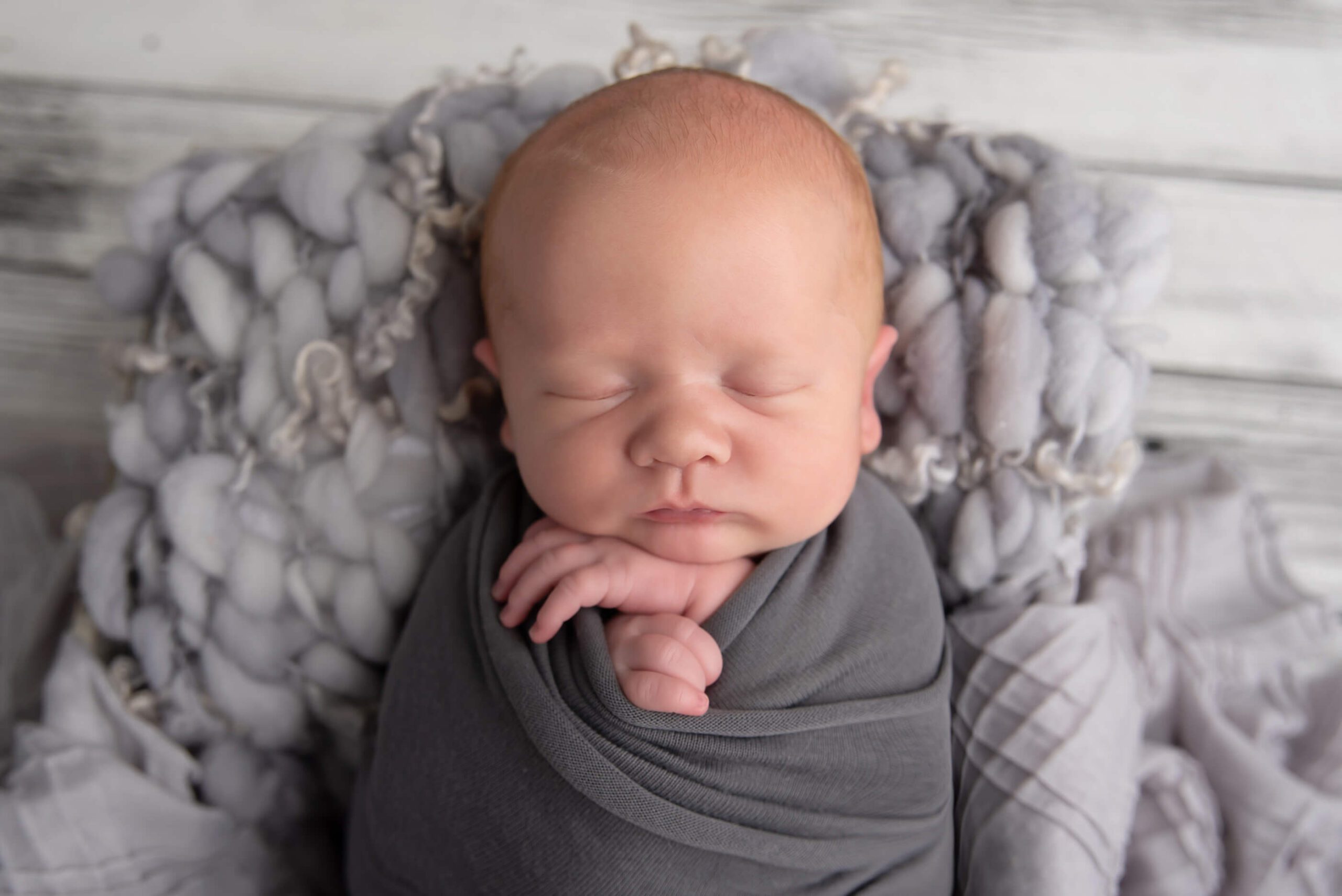 up close Burlington Newborn baby in a grey wrap with a grey wood floor
