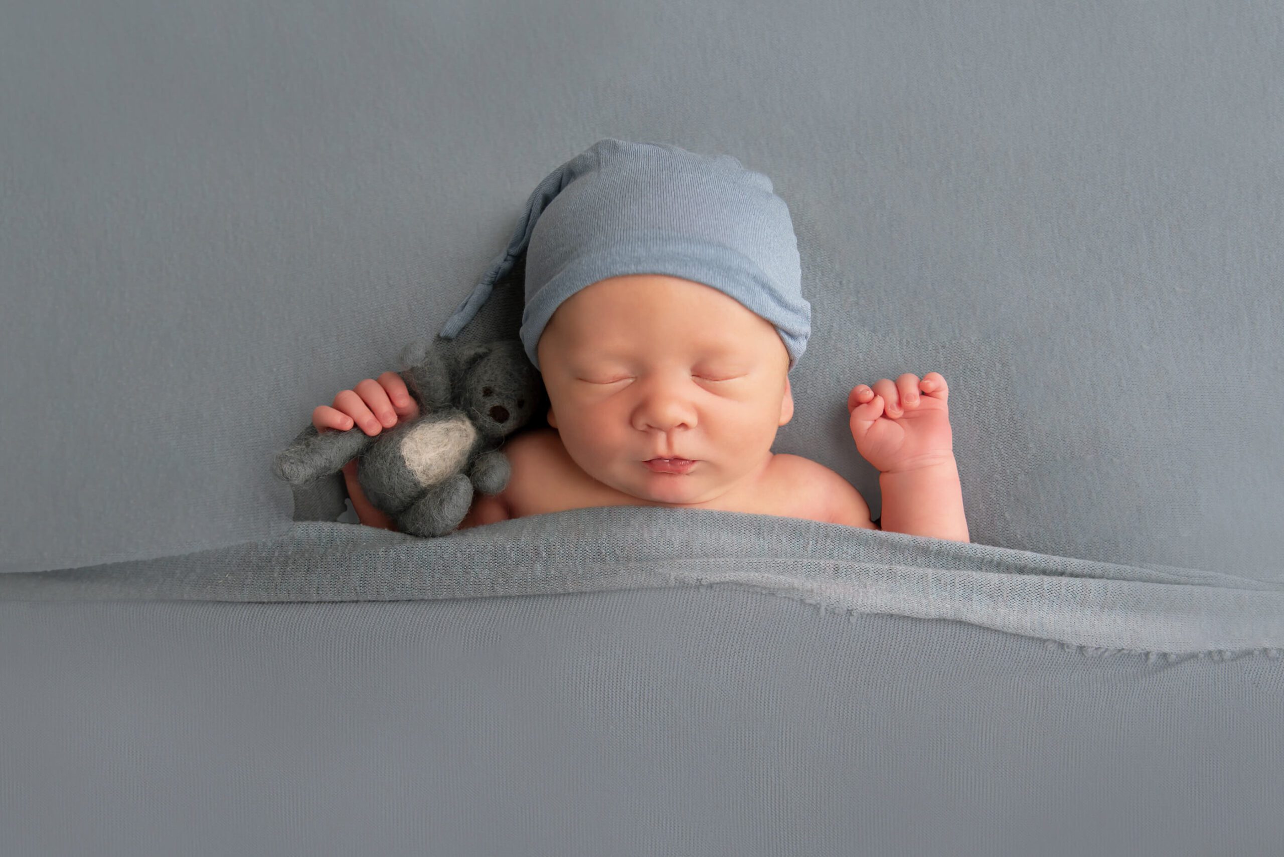 newborn photos of a boy laying with a sleepy hat and bear in hand
