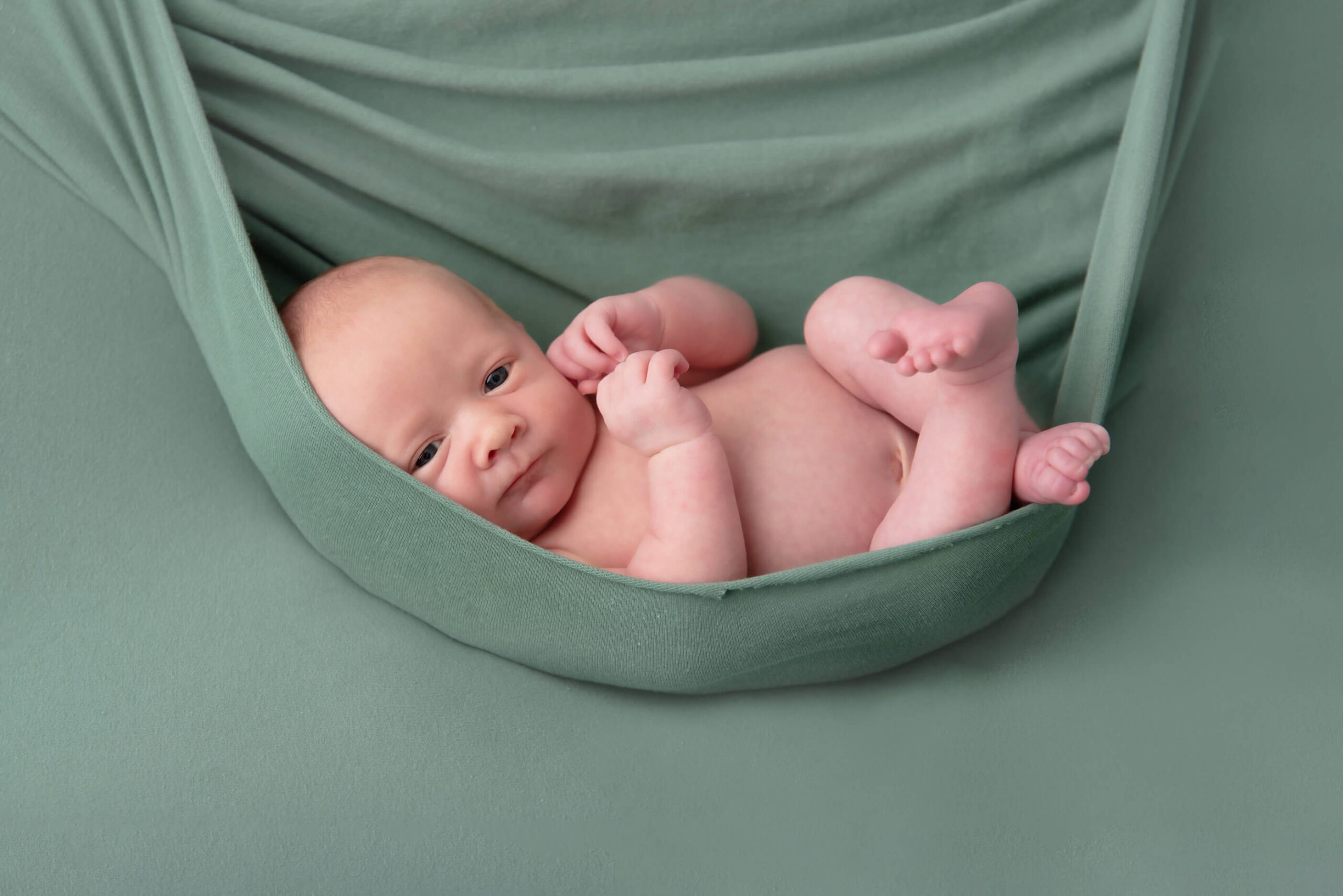 awake newborn baby boy laying in a green fabric background Burlington newborn photos
