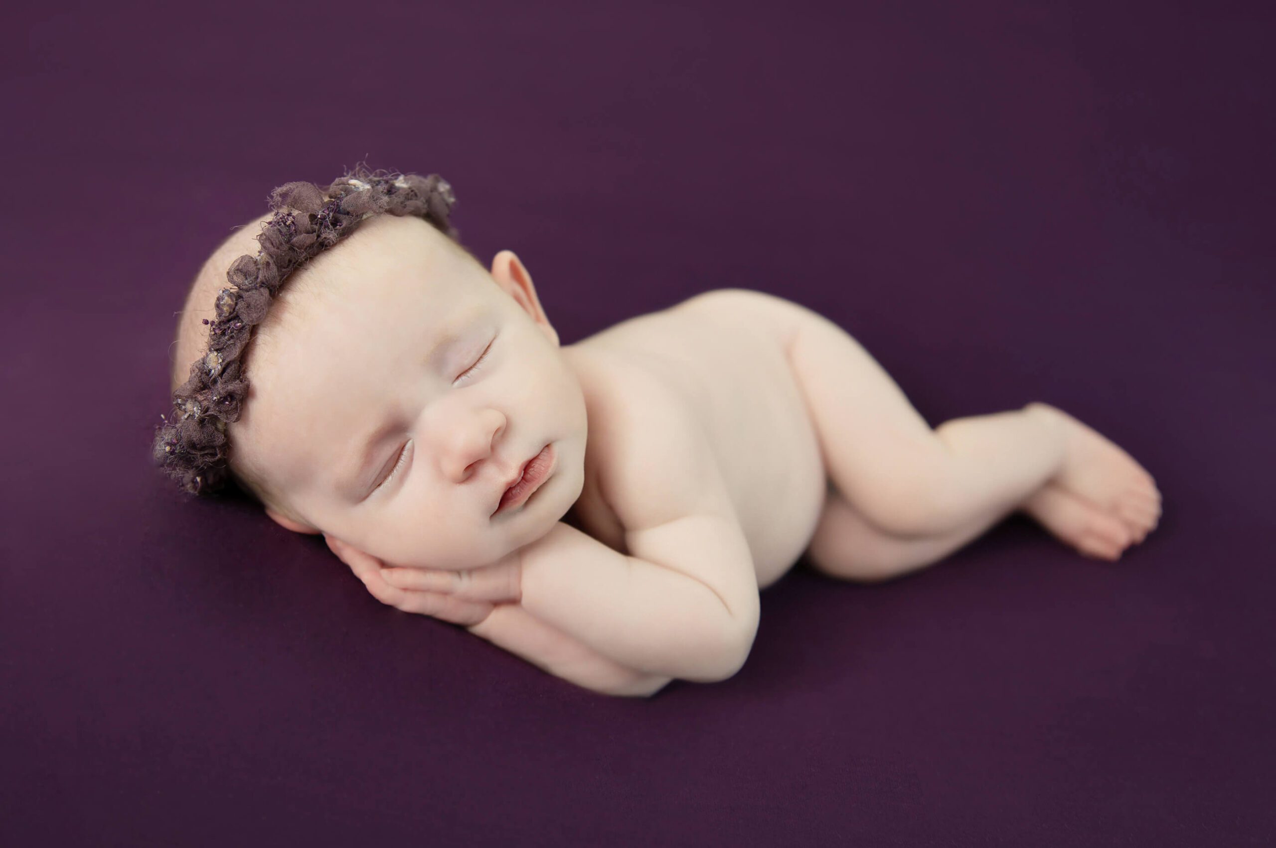 newborn baby girl laying on a purple background with purple headband Cambridge newborn photographer