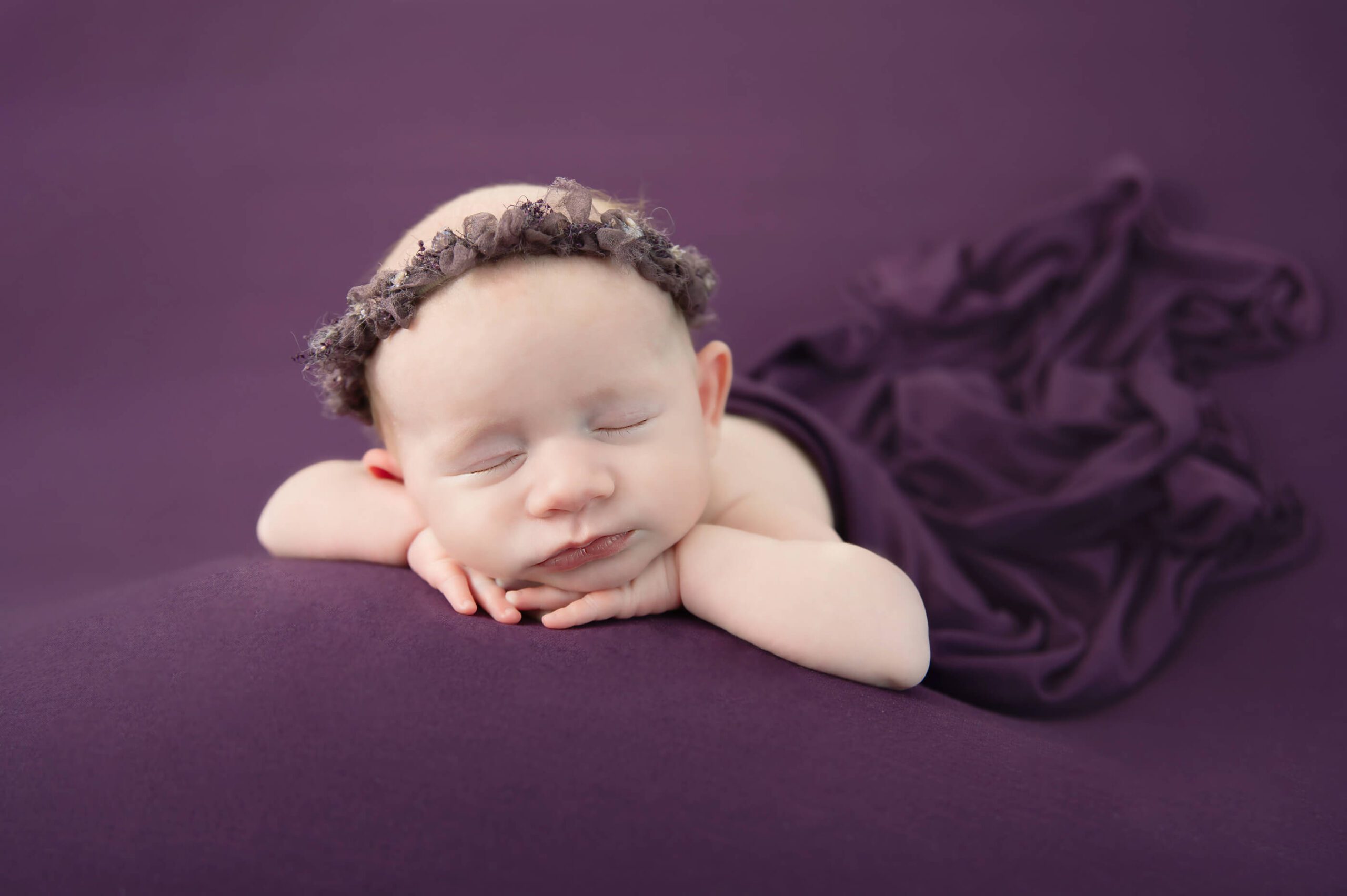 newborn baby girl laying on a purple background with purple headband Cambridge newborn photography