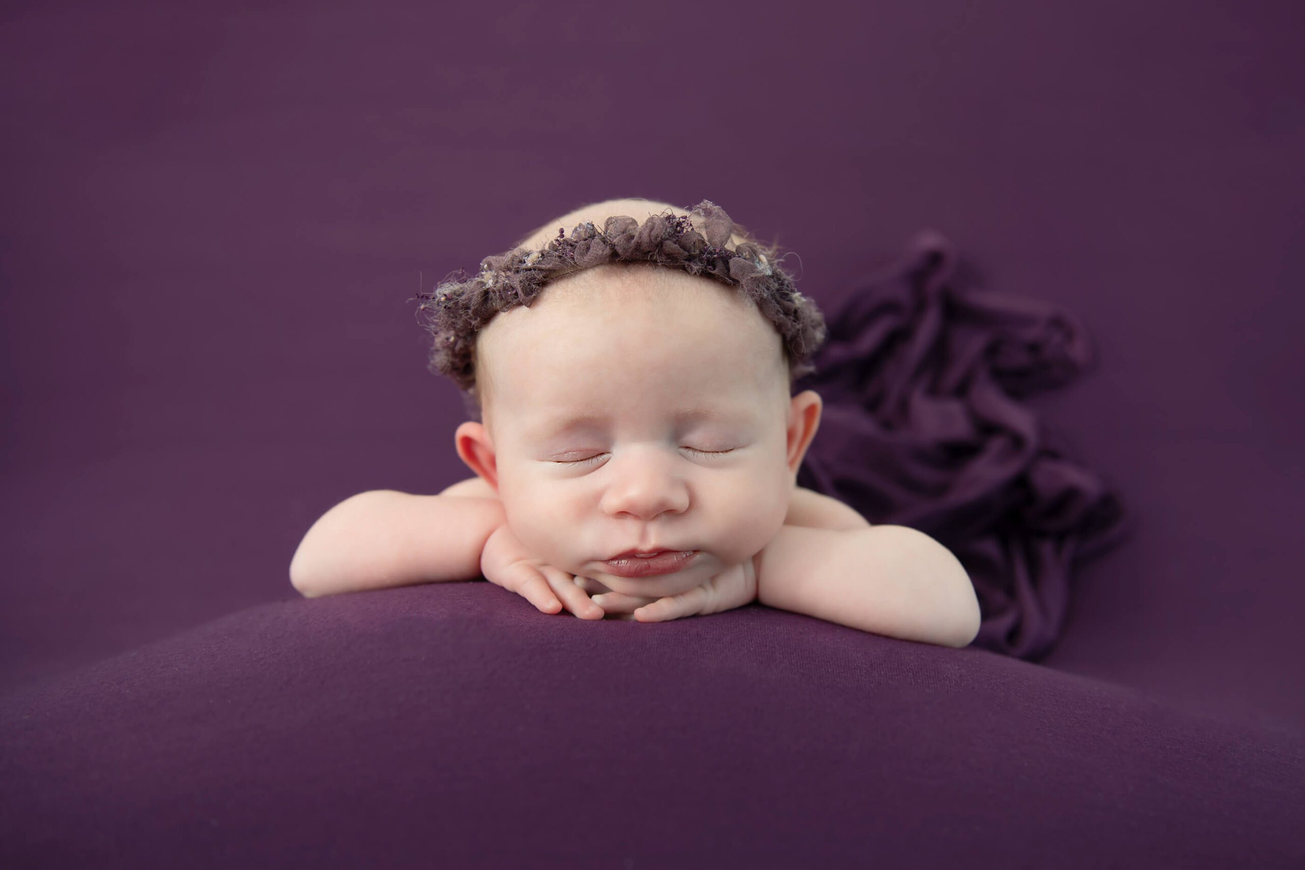 newborn baby girl laying on a purple background with purple headband Cambridge newborn photos