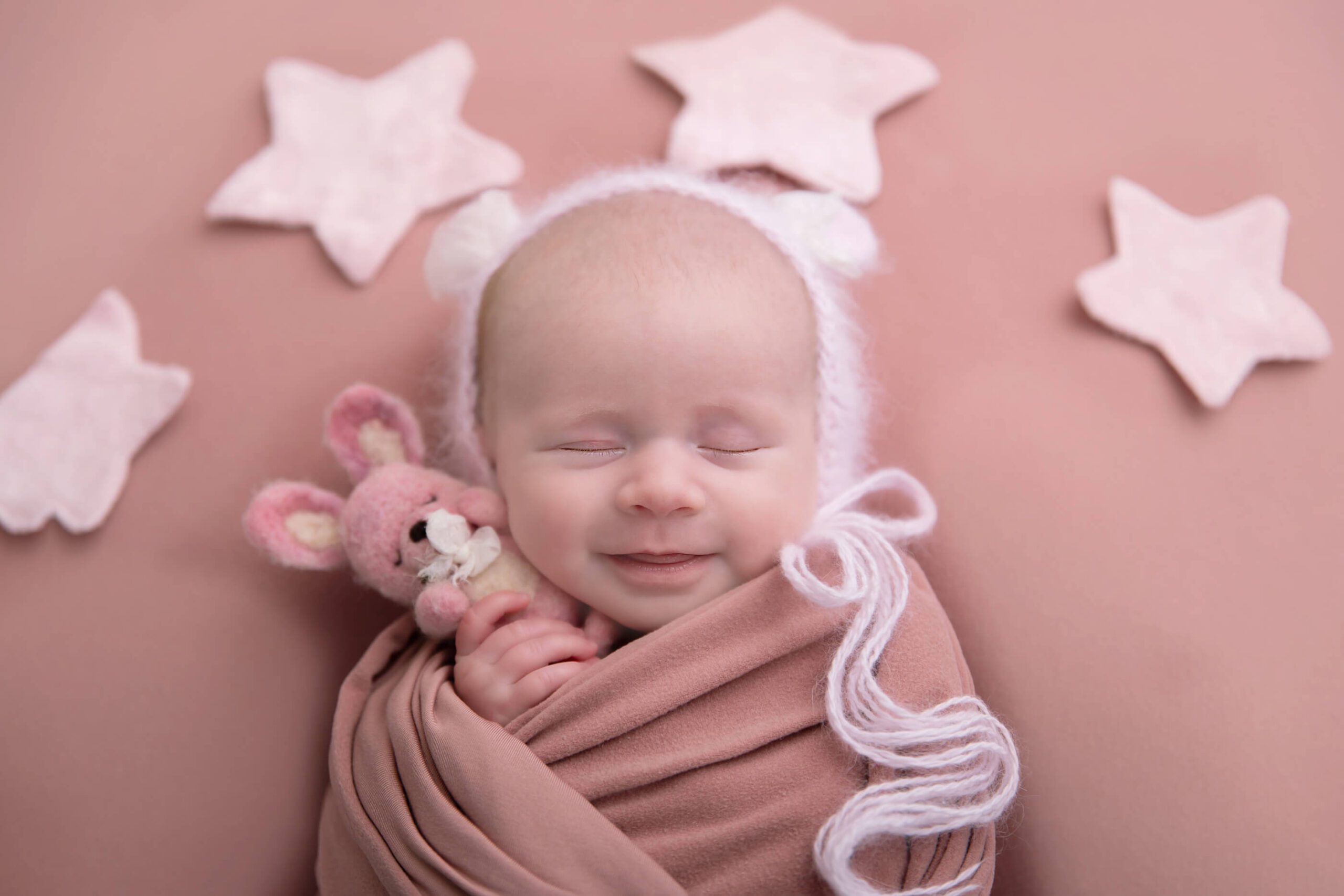 Cambridge newborn photos with girl with pink wrap and stars and bunny smiling