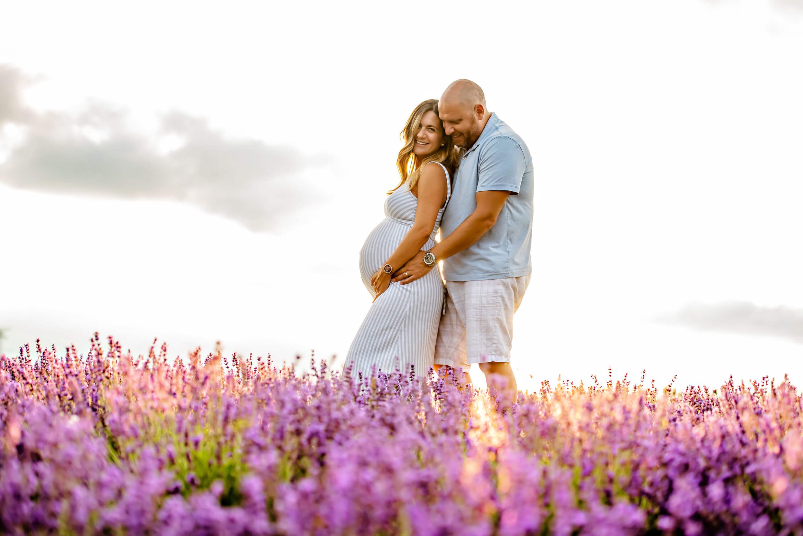 A gorgeous backlight photo of the expecting parents in the lavender field at their outdoor maternity photoshoot