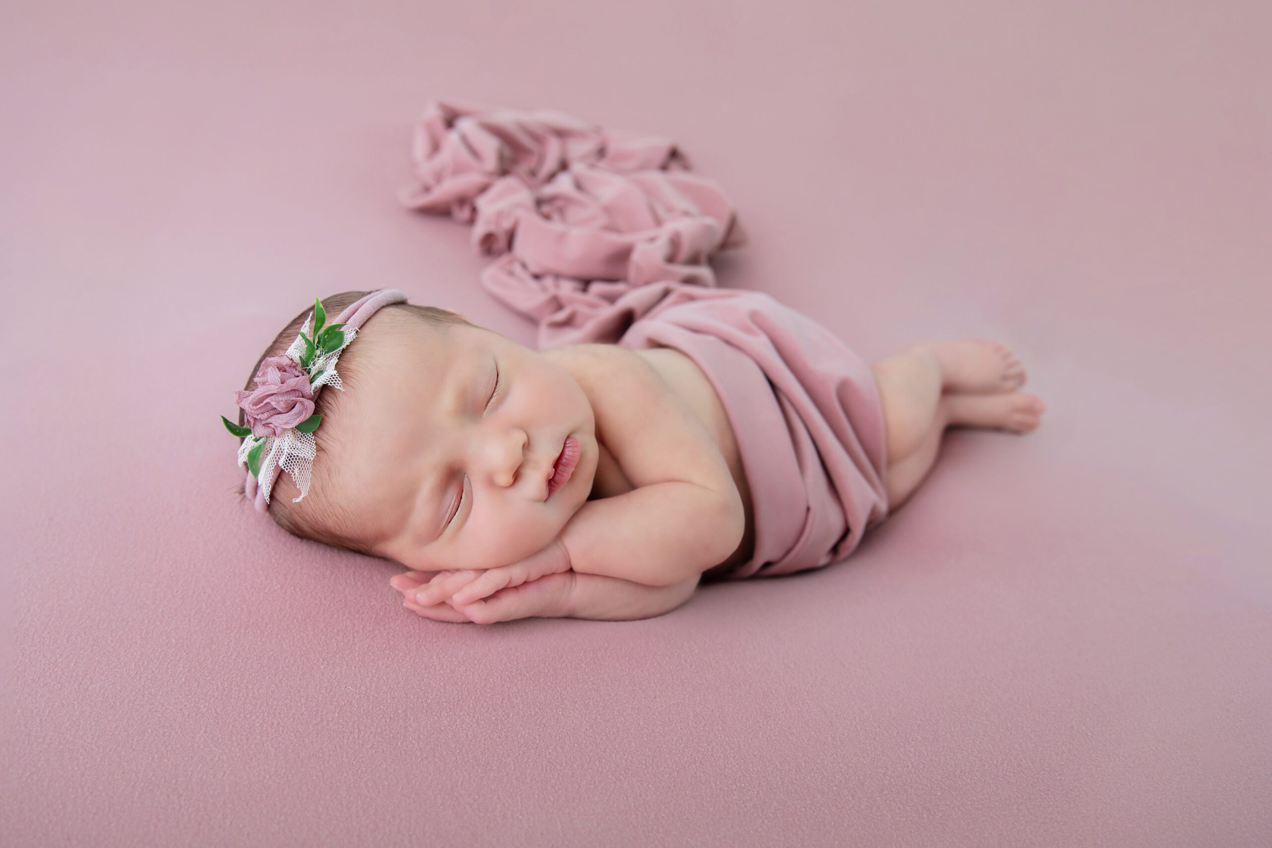newborn girl side laying on pink background