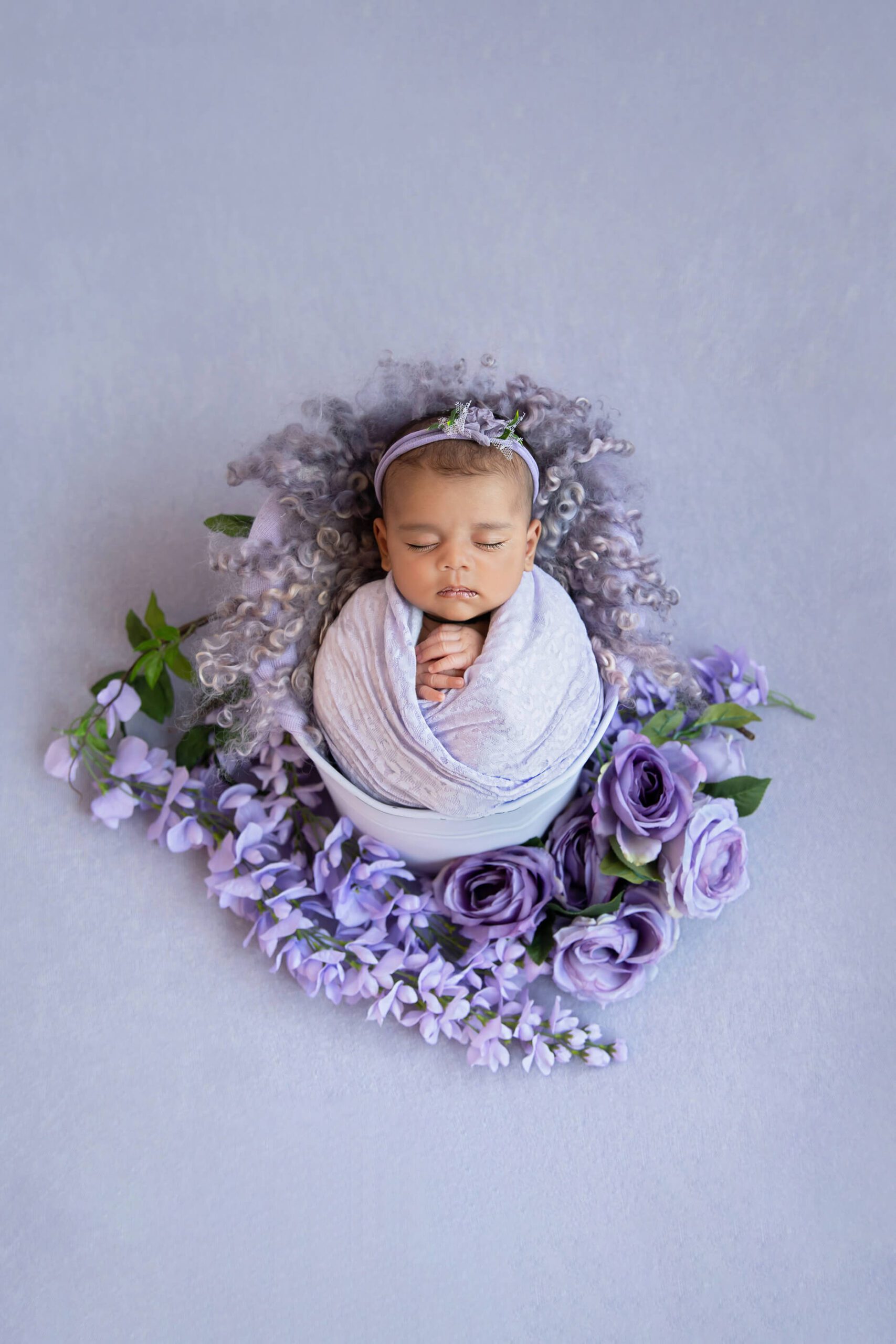 Toronto Newborn girl in purple laying in a bucket with purple flowers