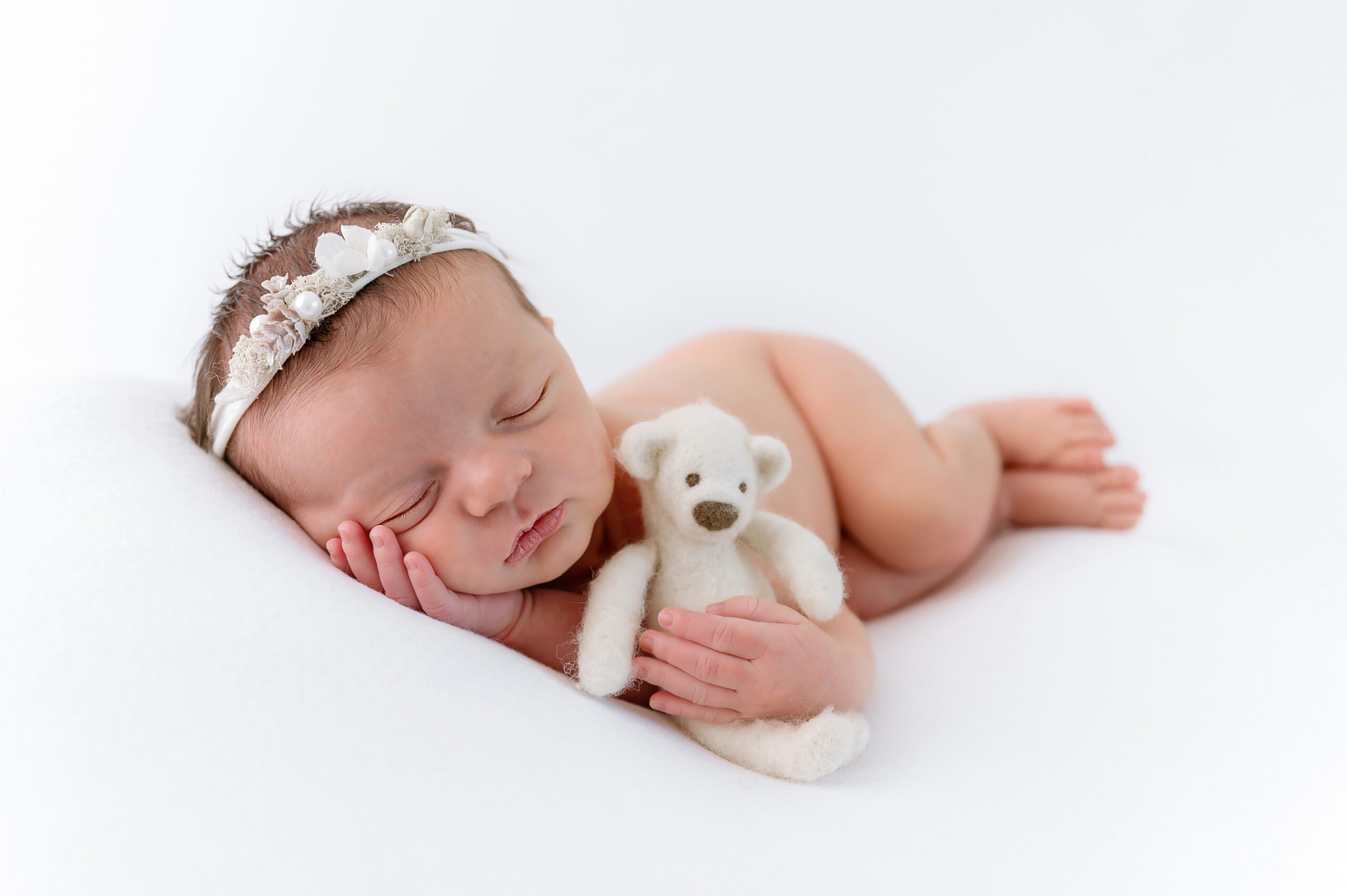 newborn girl holding a teddy bear on an all white set