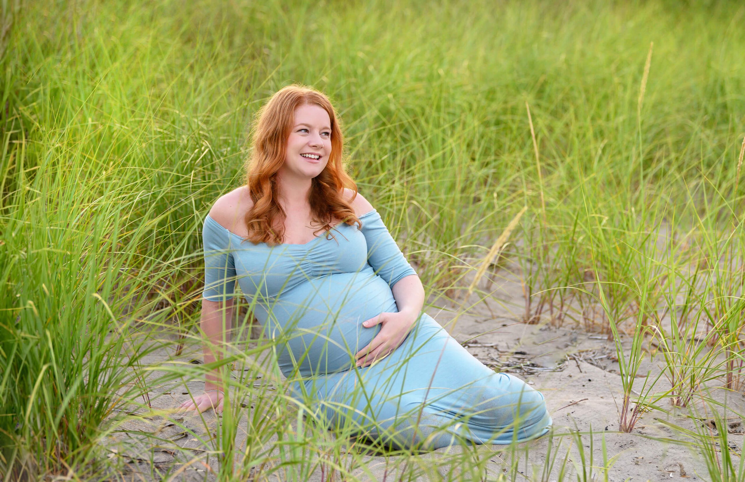 mom sitting down at the beach for her outdoor maternity photography session