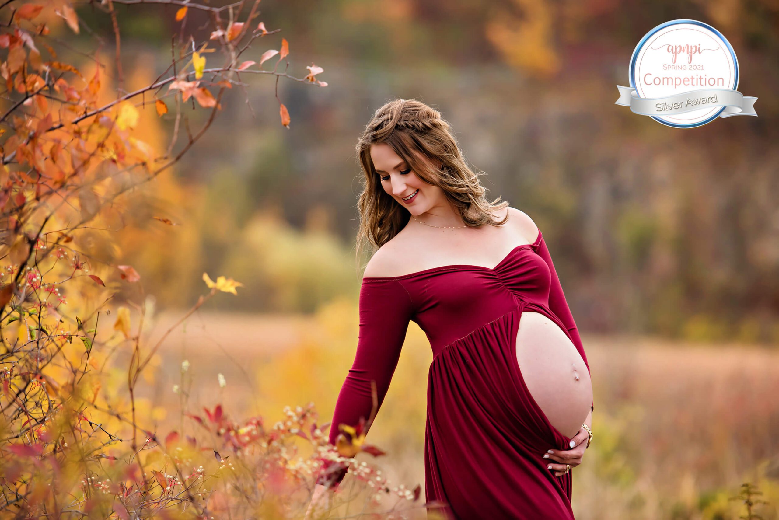 APNPI Maternity award of pregnant mom wearing a red dress showing her belly in the fall