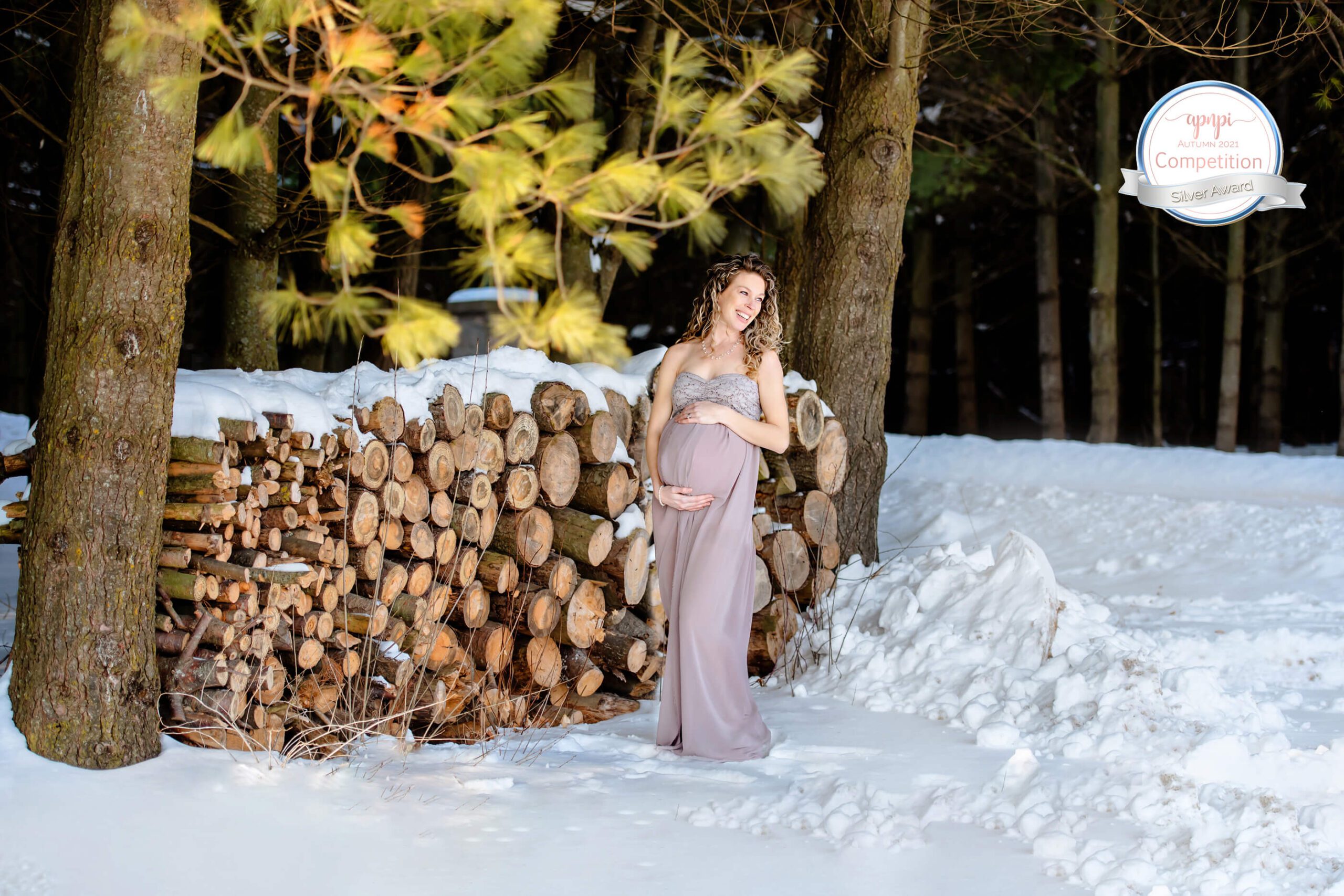 mom to be cradling her belly in the snow, smiling. Hamilton, Ontario Maternity Photographer