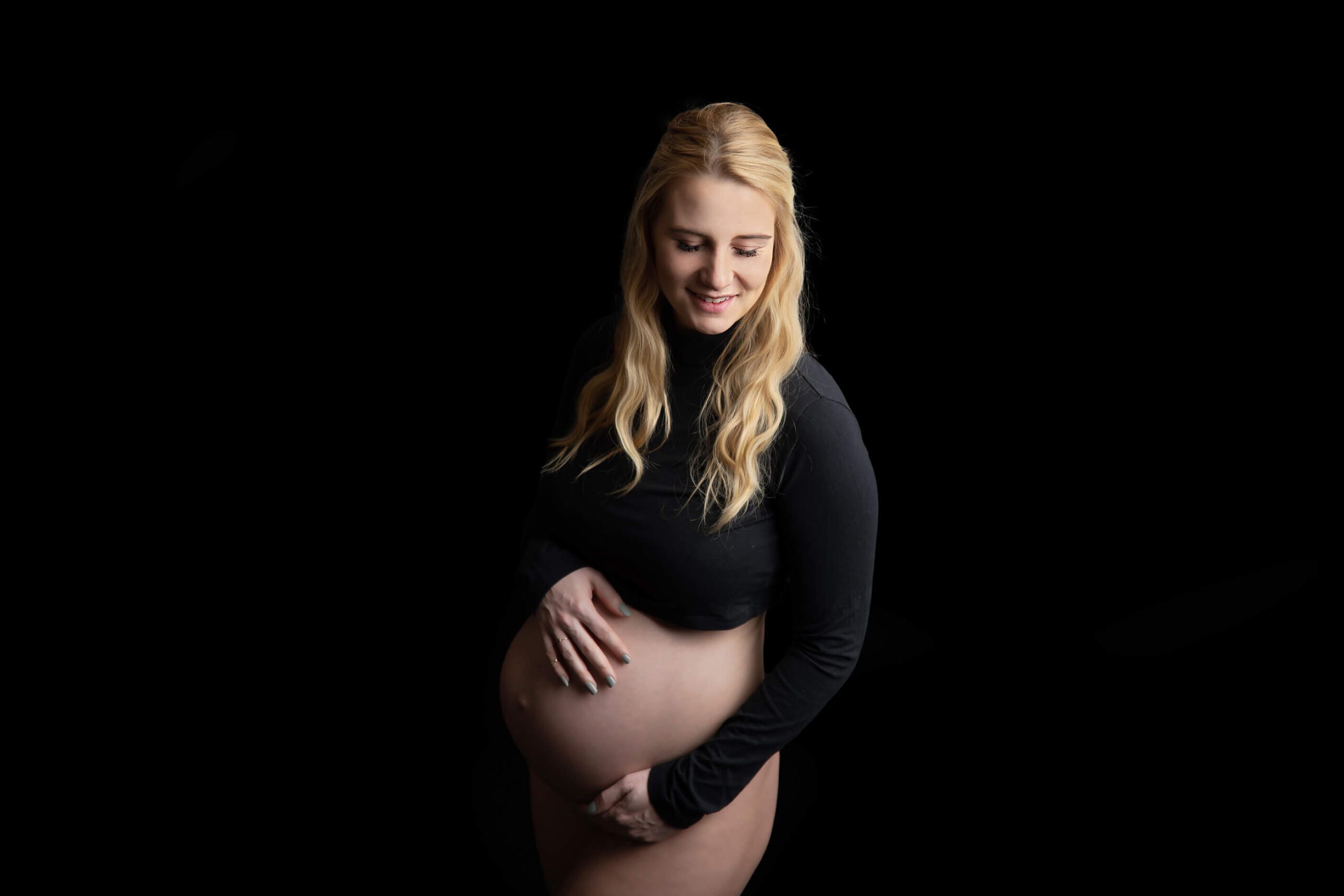 All black studio maternity photography session mom with blonde hair holding belly and smiling baby shower venues Hamilton Ontario