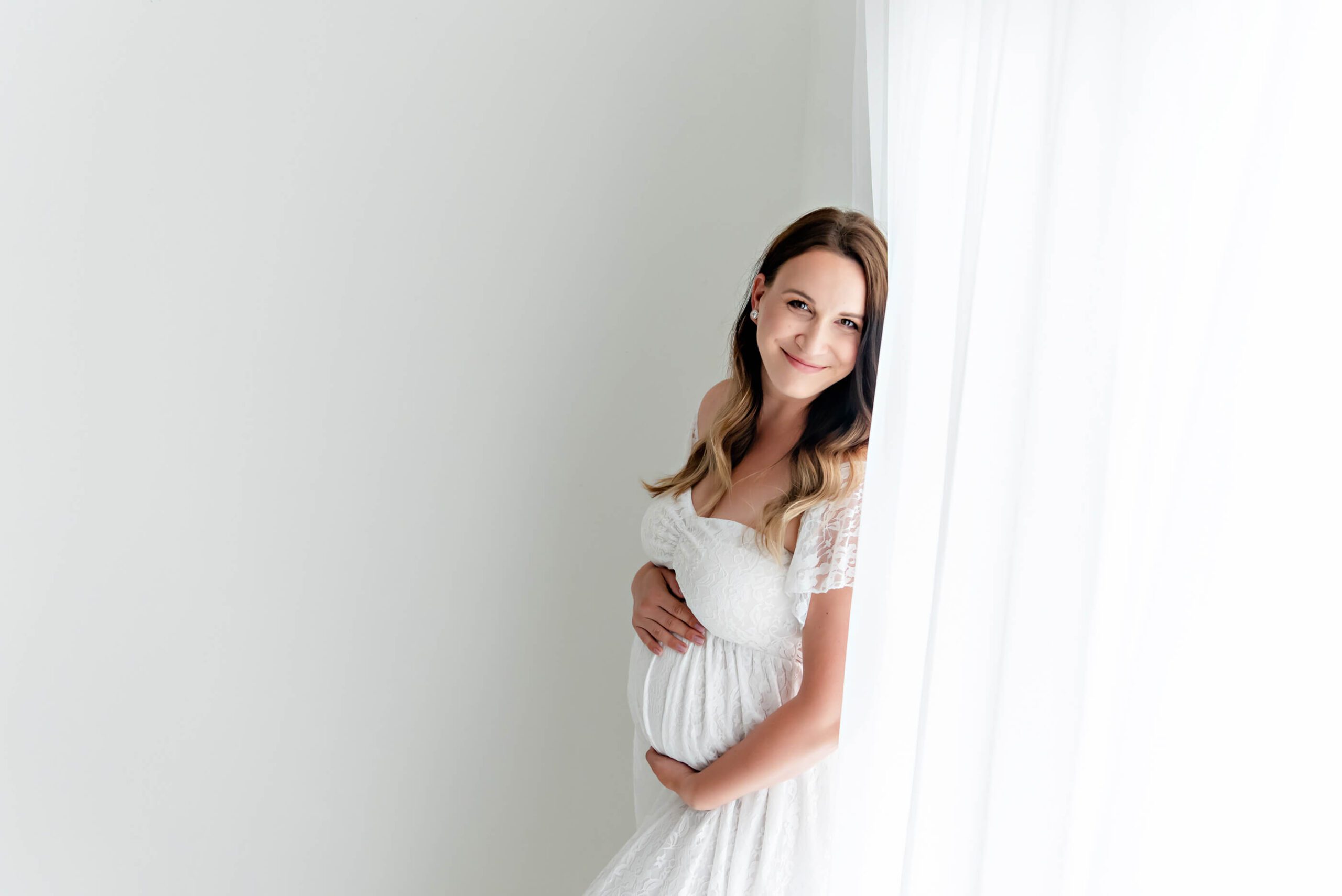 Burlington, Ontario studio maternity session mom in all white smiling holding her belly