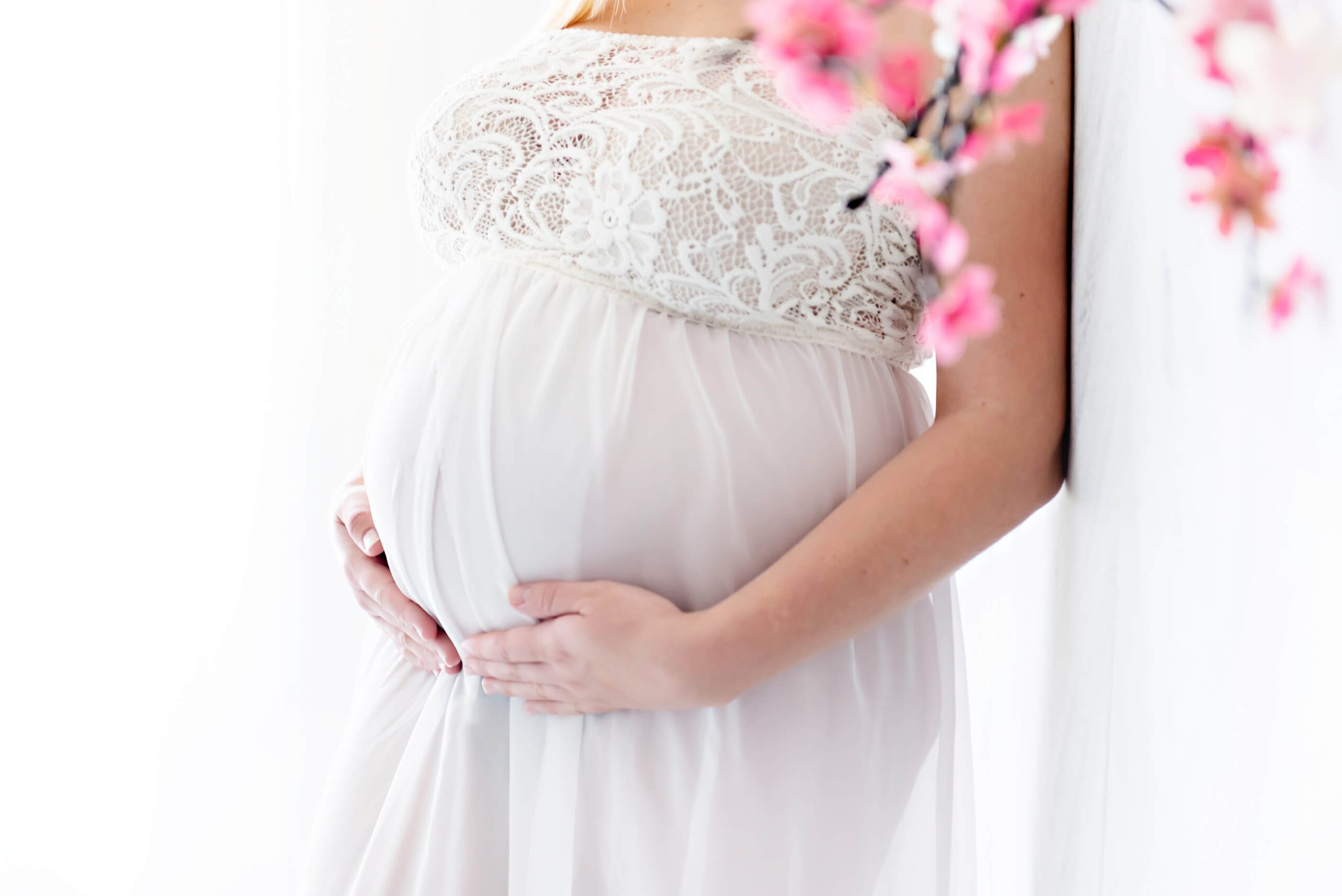 close up photo with mom holding her belly with cherry blossom photos in the frame