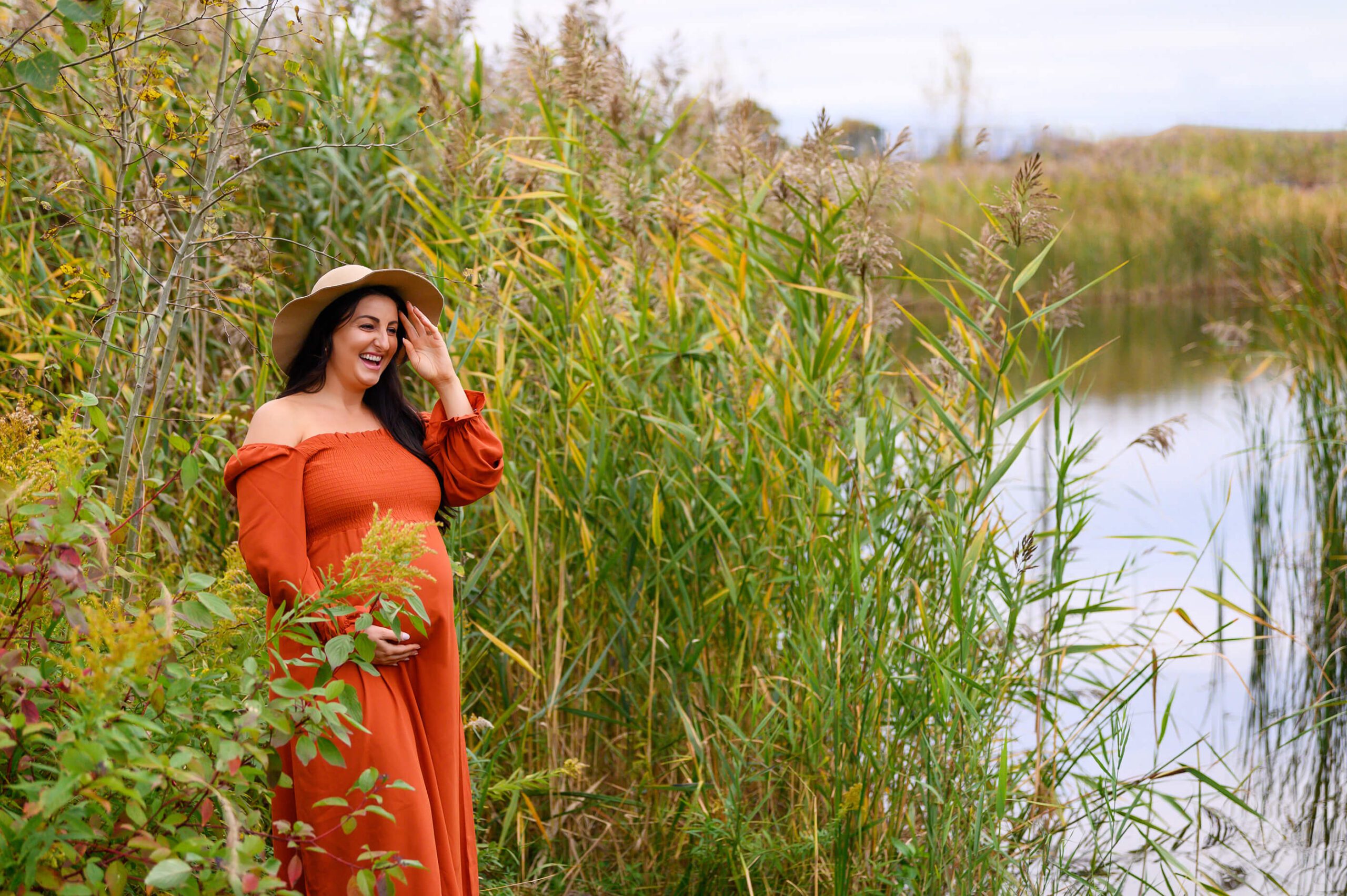 Mom smiling holding her hat her baby belly wearing an orange dress. Toronto Pelvic Floor Physiotherapy 