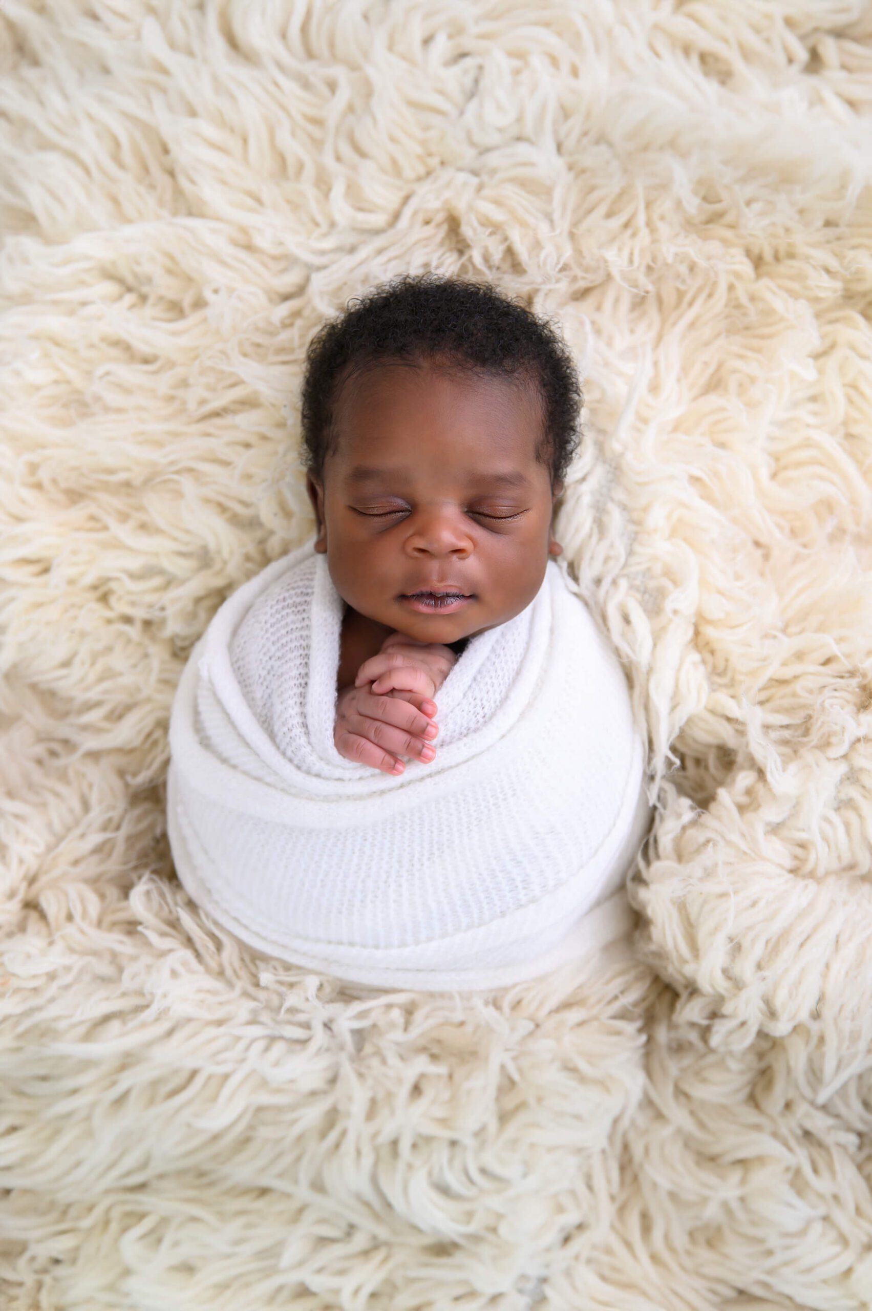 newborn photos of a little boy wrapped in white on a cream rug