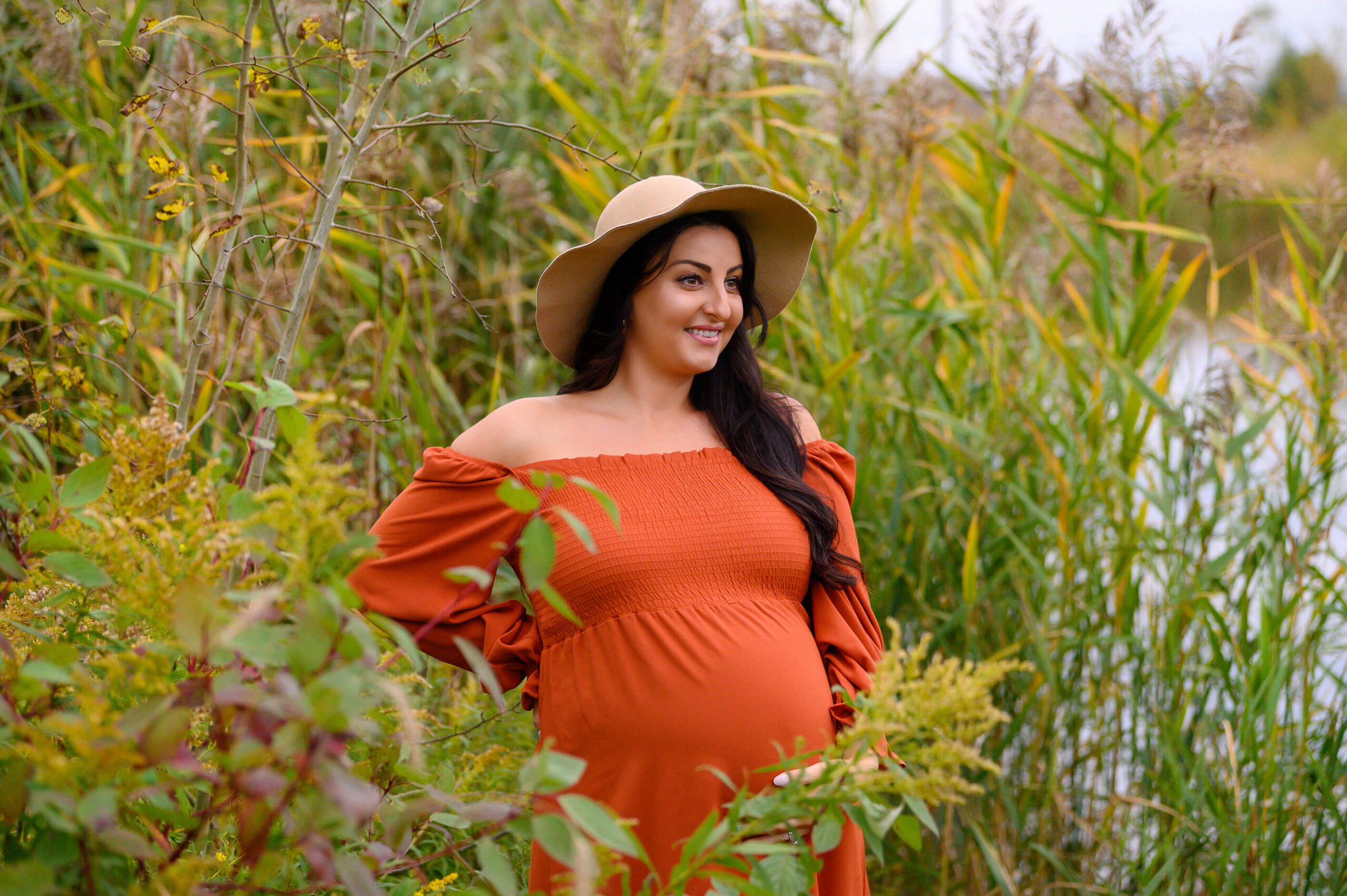 outdoor maternity photography session wearing an orange dress wearing a hat