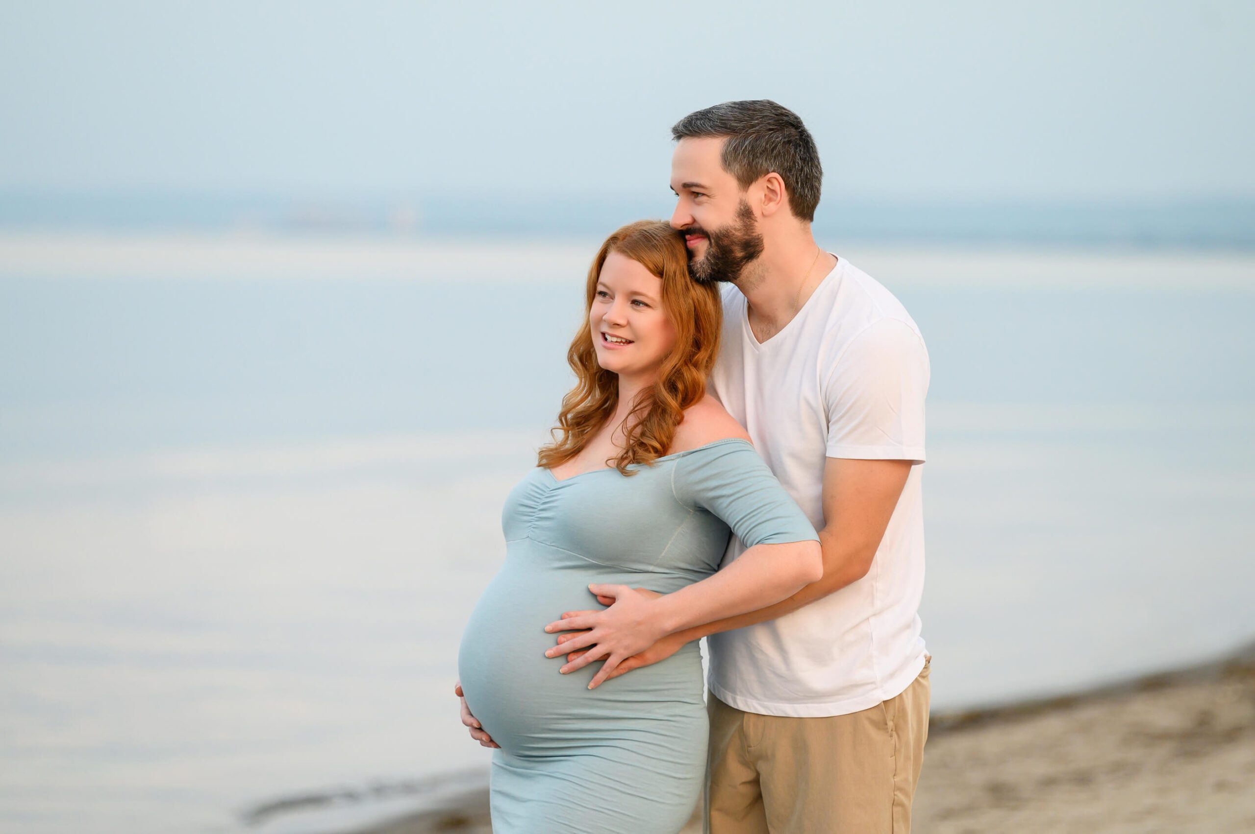 husband and wife at their beach maternity session smiling gazing into the water