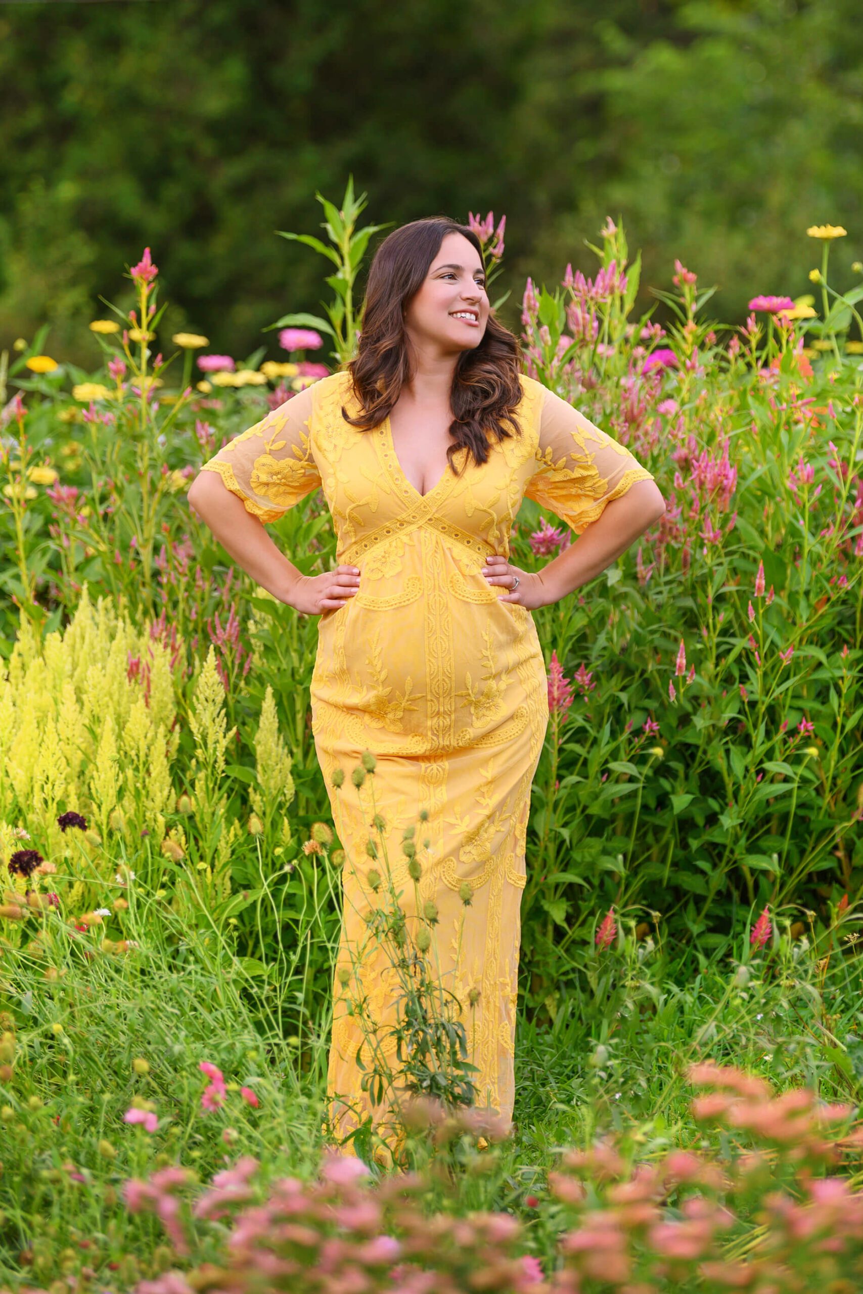maternity mom with her hands on her hips smiling wearing a yellow dress
