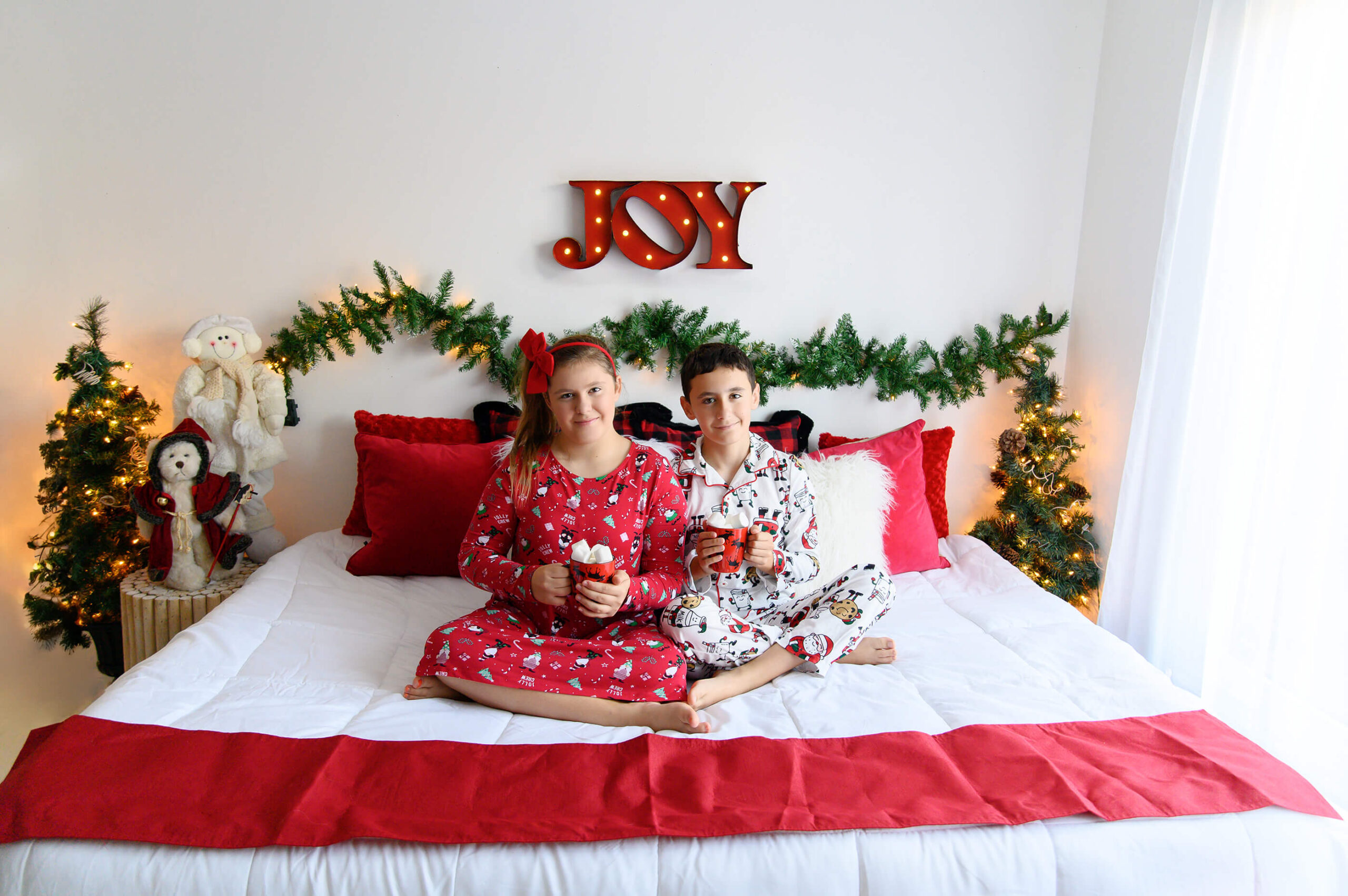 brother and sister sitting on a bed with red and white christmas colours in their pjs.