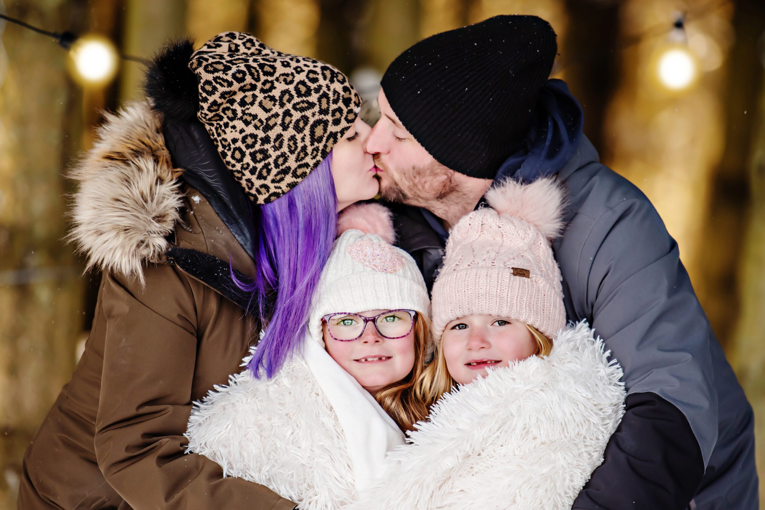 Mom and dad kissing with two daughter standing in front