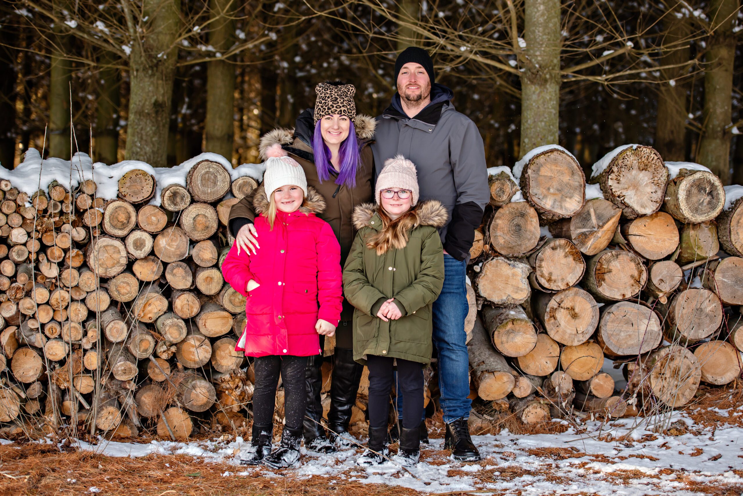 Mom and dad with two daughters standing in front of hundreds of cut logs in a winter forest for their winter activities Toronto 