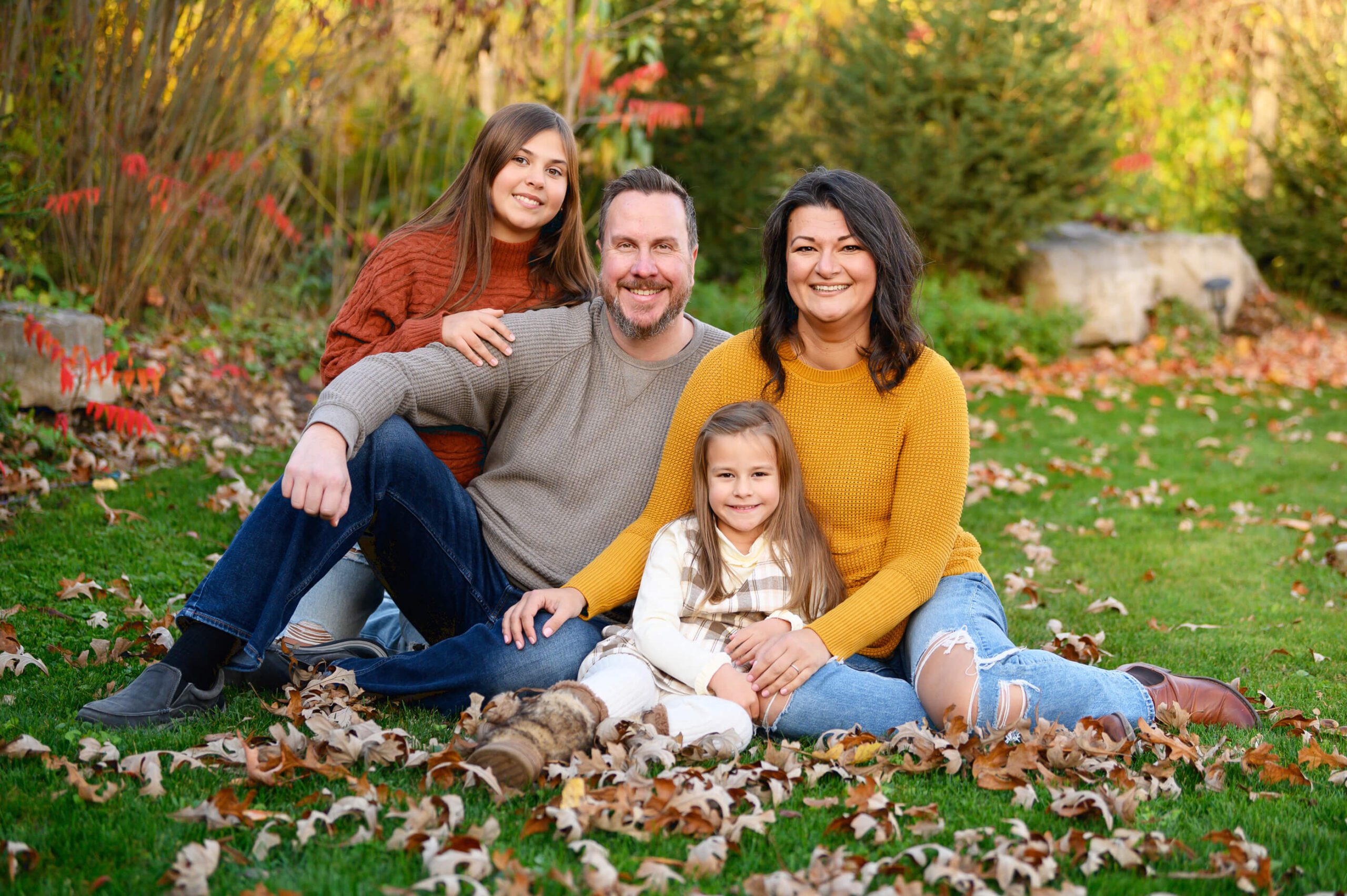 Mom and dad with two daughters sitting on the ground with leaves all around for their Toronto Family Photography session.