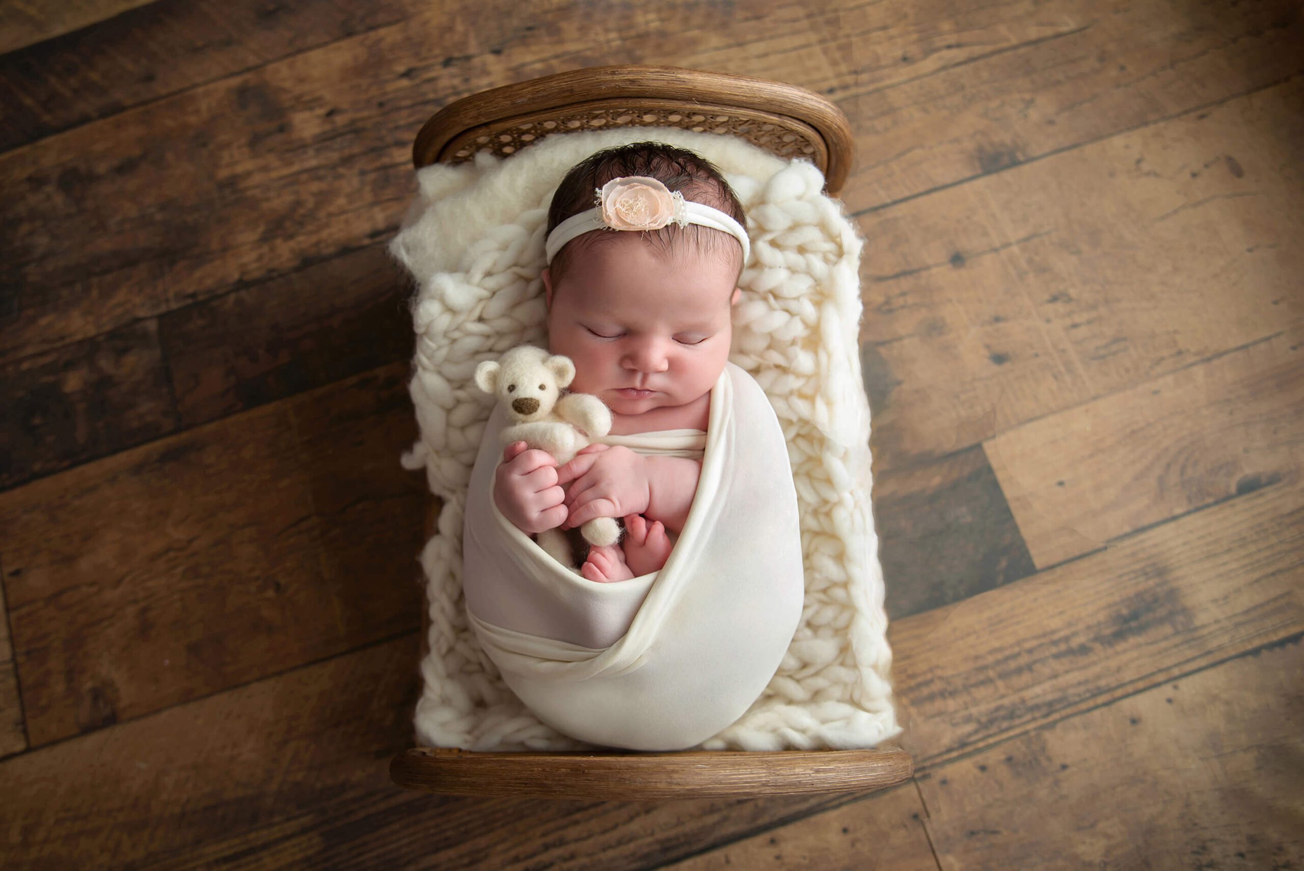 Newborn baby holding a teddy bear laying on a bed. Baby shower venues Burlington, Ontario.