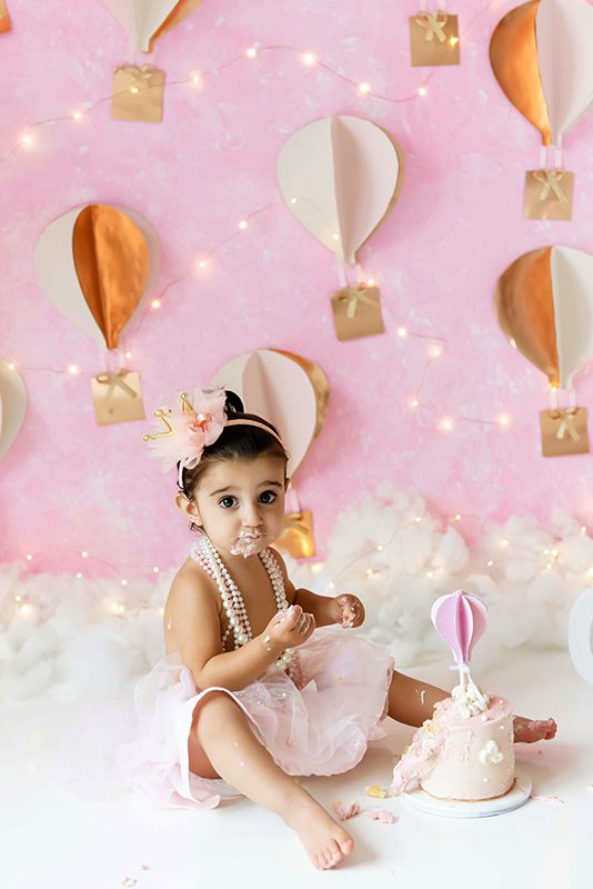 Little girl in a pink tutu and pearls for her hot air balloon Burlington cake smash photography session.