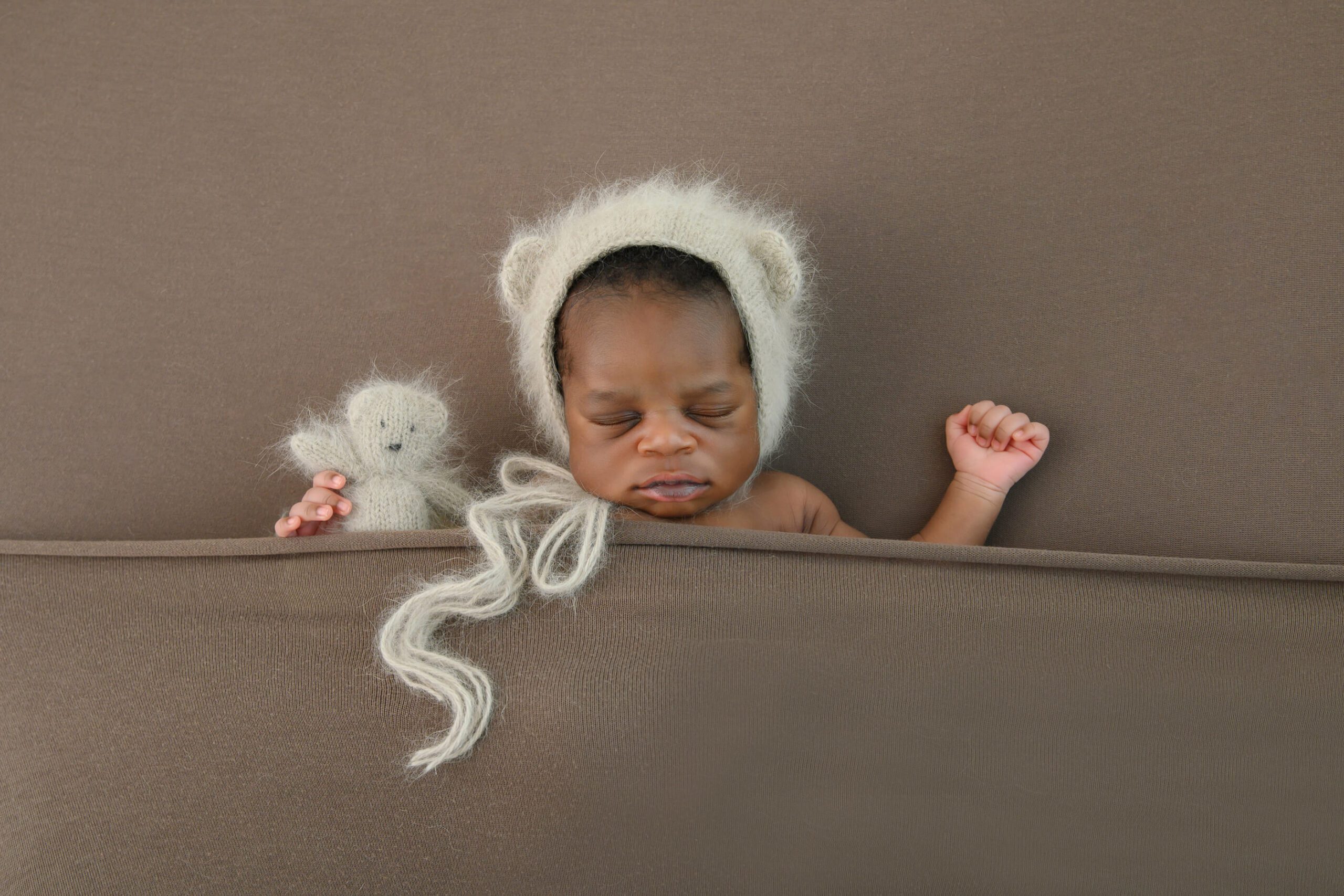 newborn baby boy in a bear hat holding a little teddy bear all brown colours. Toronto Newborn Photographer.