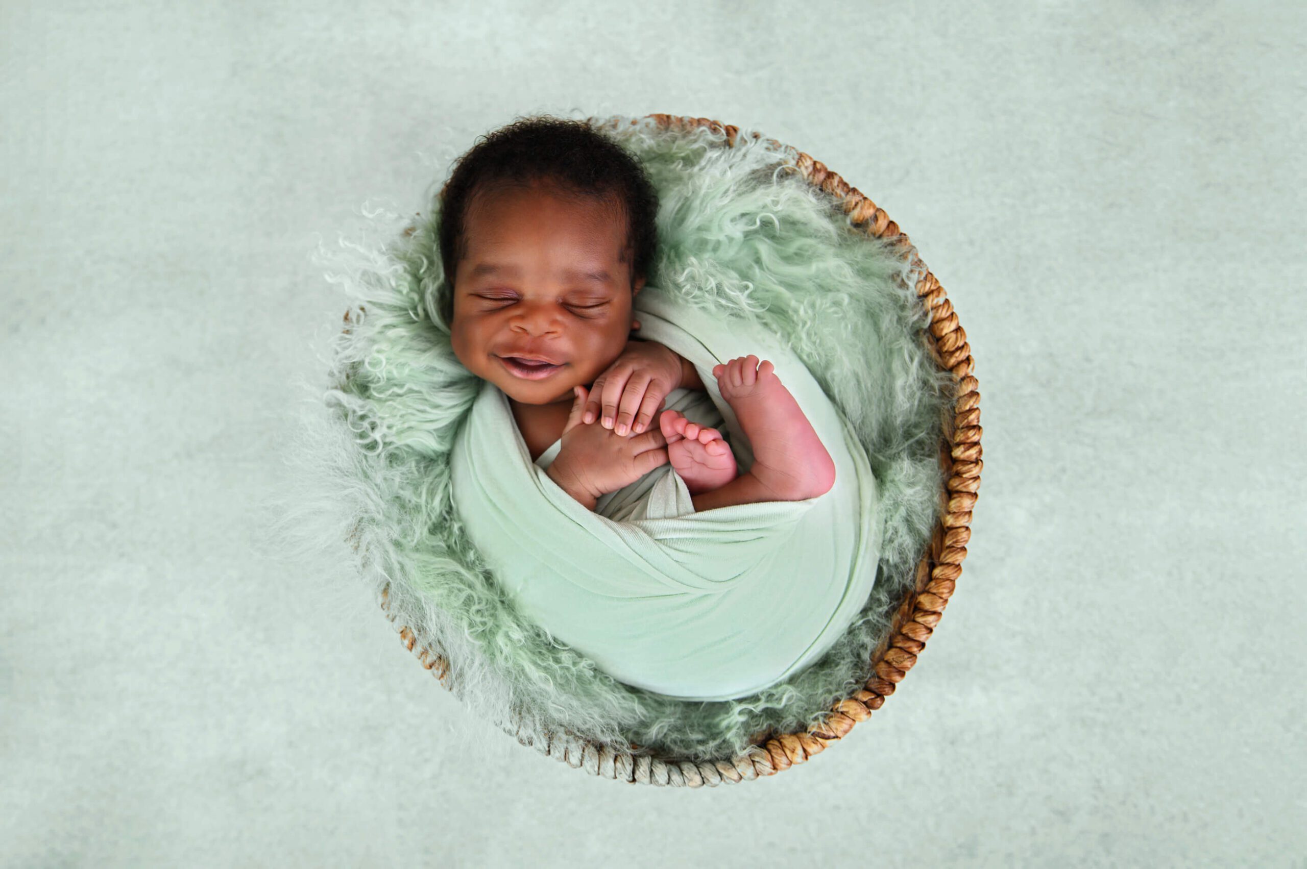 Newborn baby boy smiling in a mint green warp and fur rug.