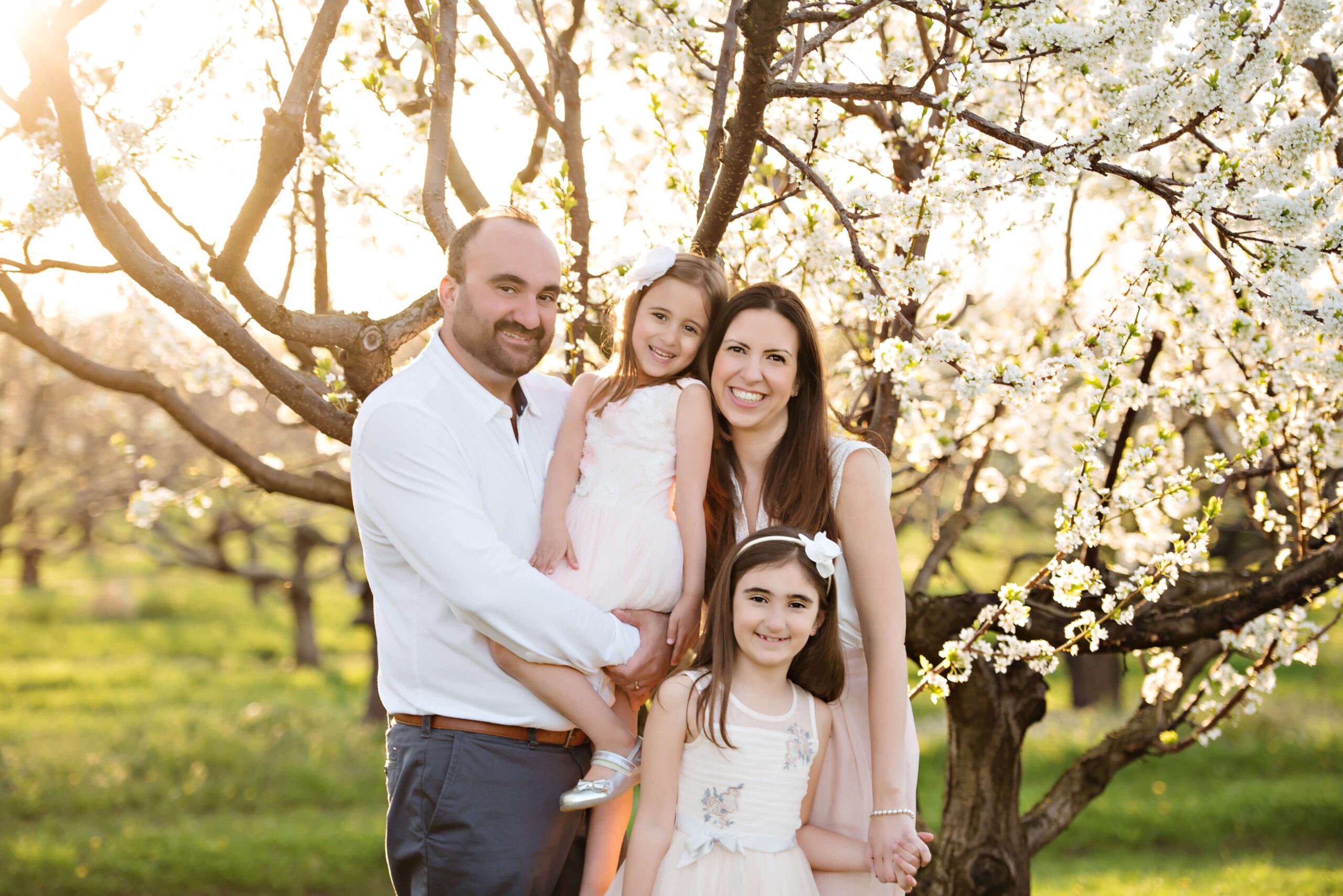 family of four with two girls with the white blossom orchard.