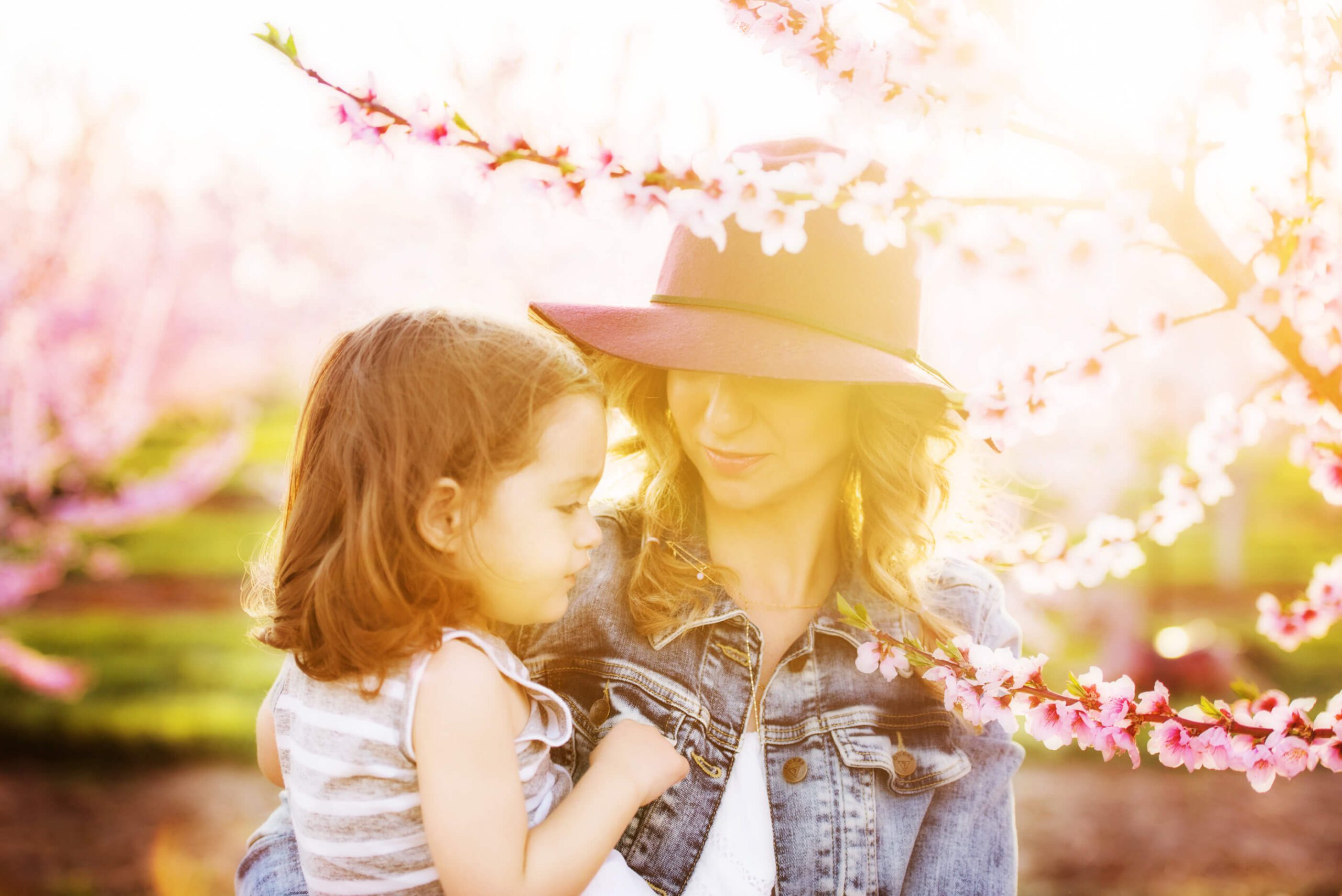 Mom hold her daughter wearing a fushia hat with the golden light shining from behind on both of them.