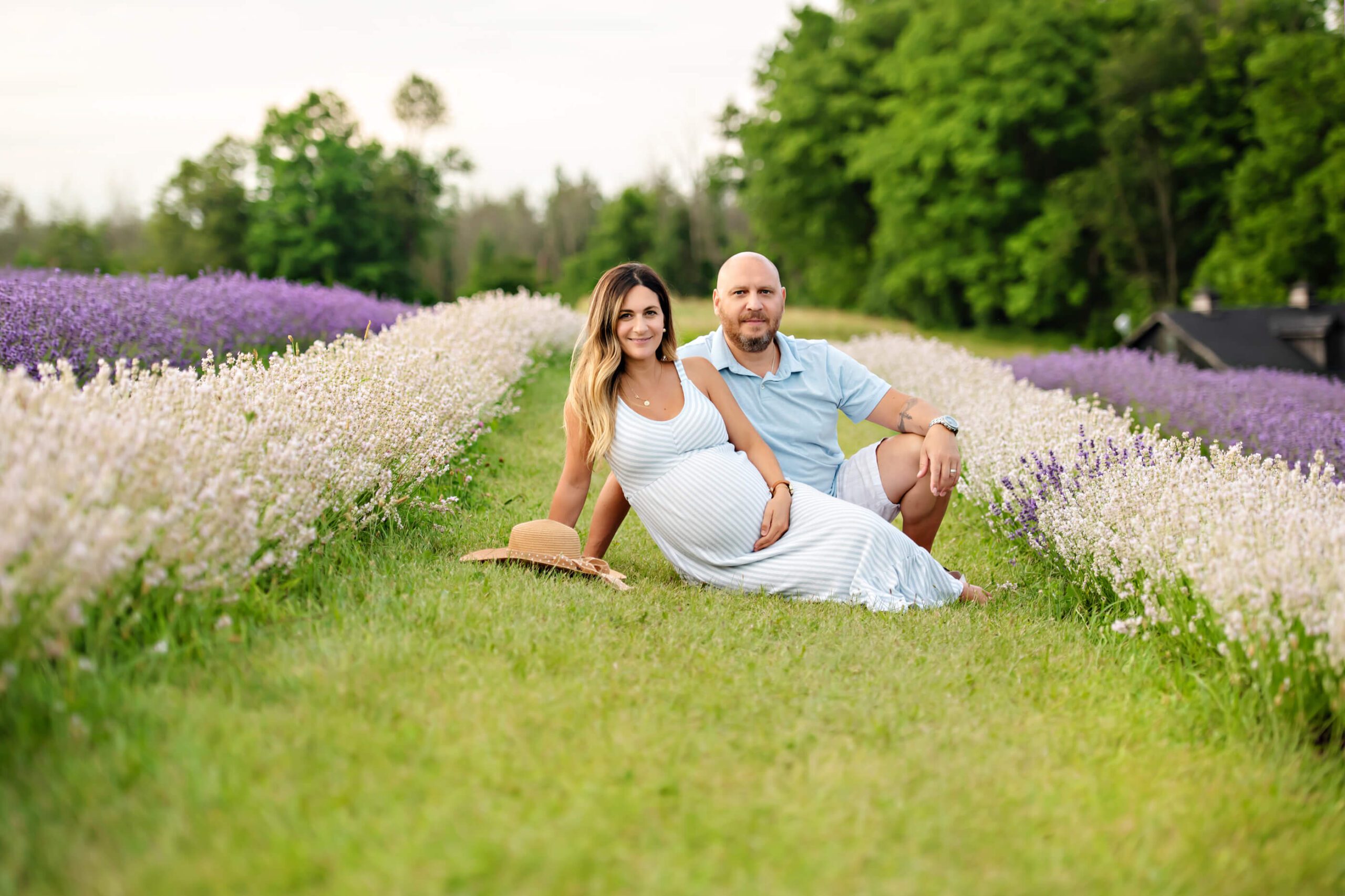 Outdoor Lavender Farm near Toronto Maternity photo of a mom and dad sitting on the grass amongst the white and purple lavender.